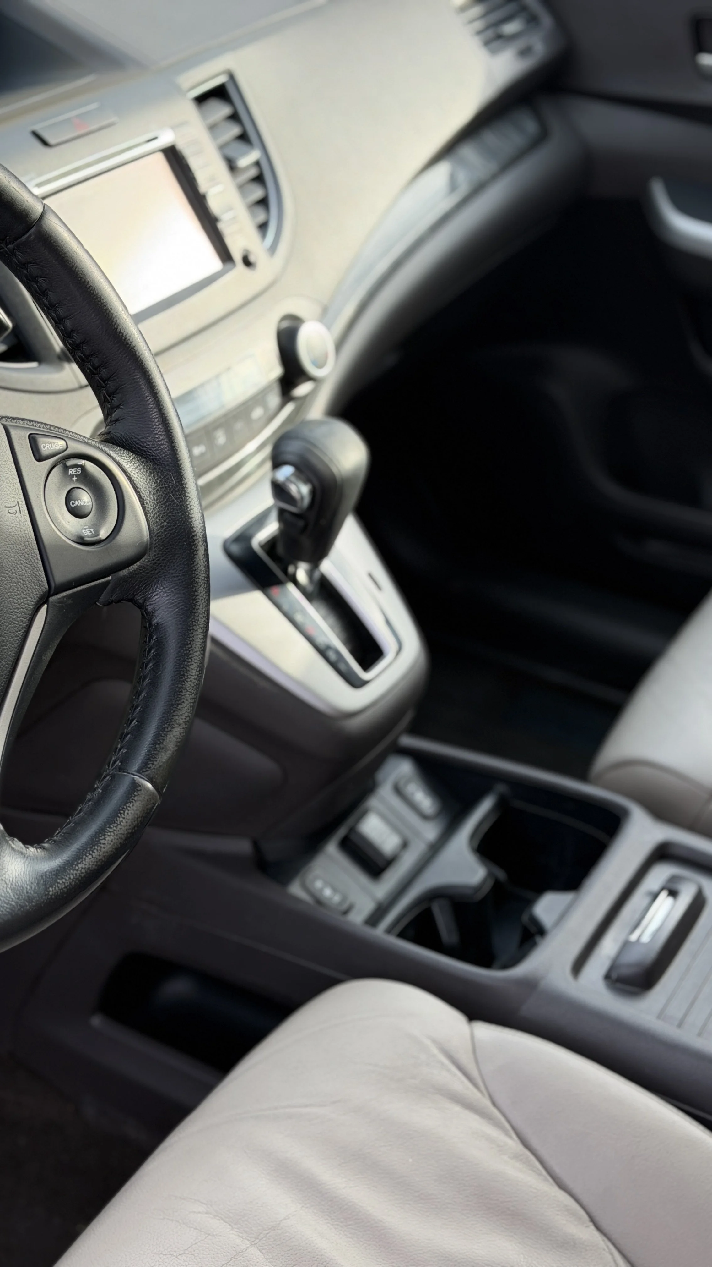 Interior of a car showing a black leather steering wheel, gear shifter, dashboard, and beige driver's seat.