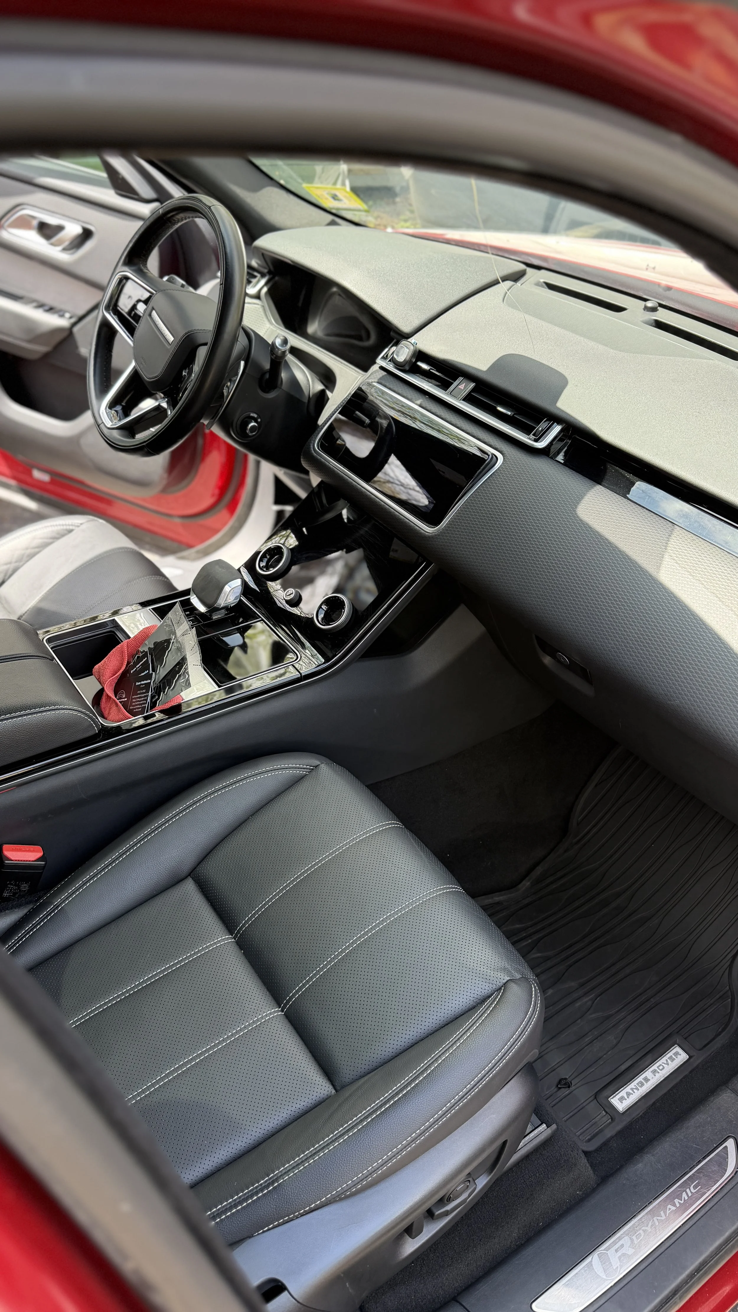 Interior of a modern red Range Rover vehicle, showing gray leather front seats, a central console with a gear shifter and touchscreen display, and black dashboard with air vents.