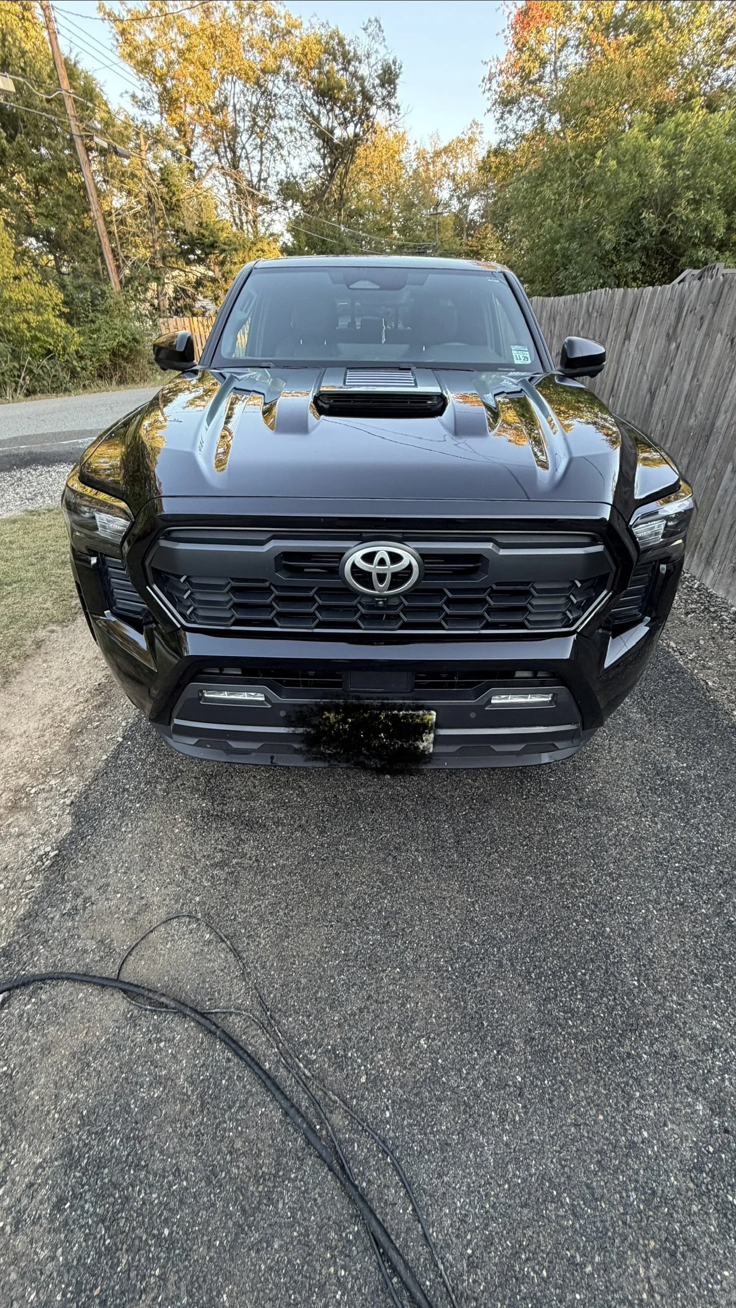 Front view of a black Toyota SUV parked outdoors on a gravel surface with trees and a wooden fence in the background.