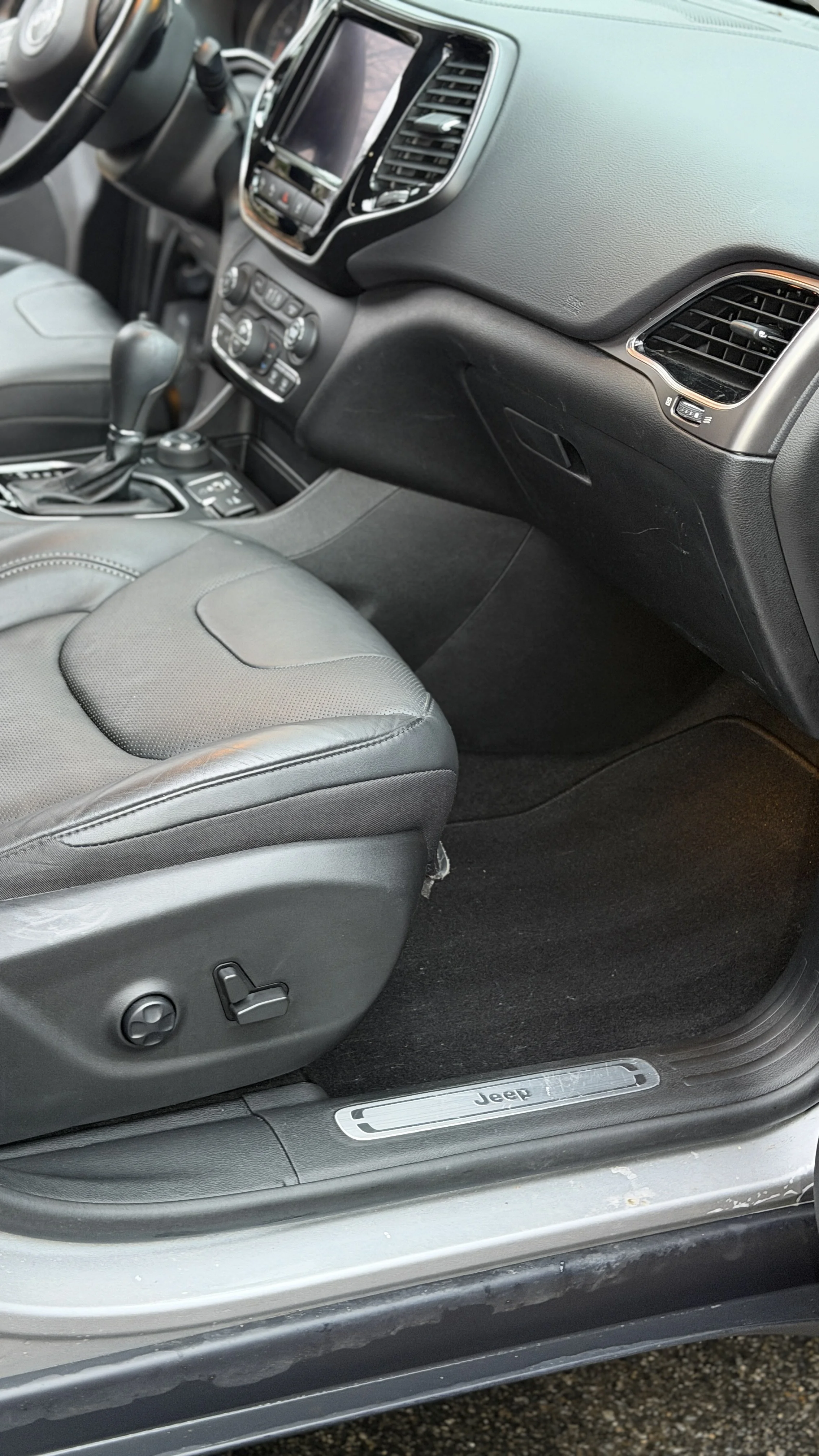 Close-up of the interior of a Jeep vehicle showing the passenger seat, dashboard, center console, and door sill with Jeep logo.