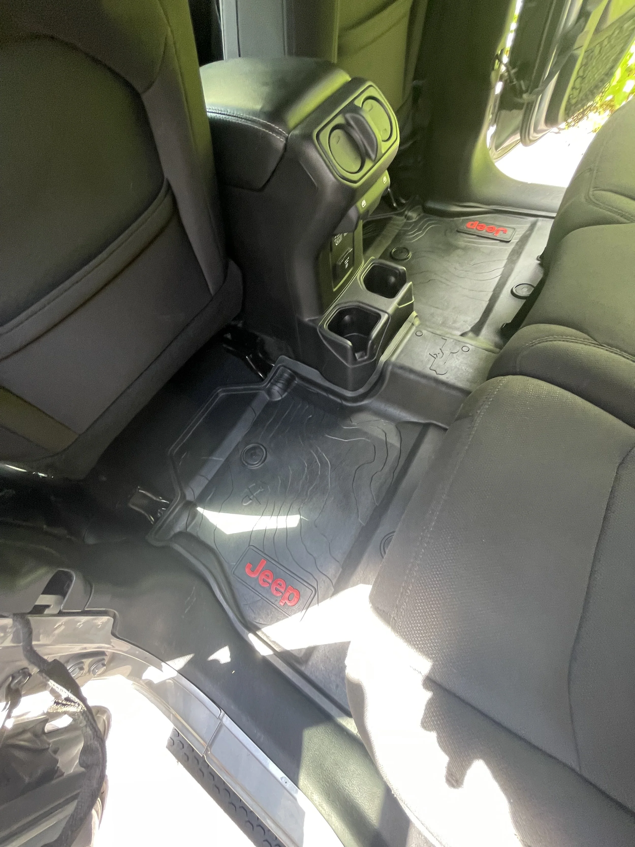 Interior of a Jeep vehicle showing the back seats, rear center console, and floor mats with red Jeep logo.