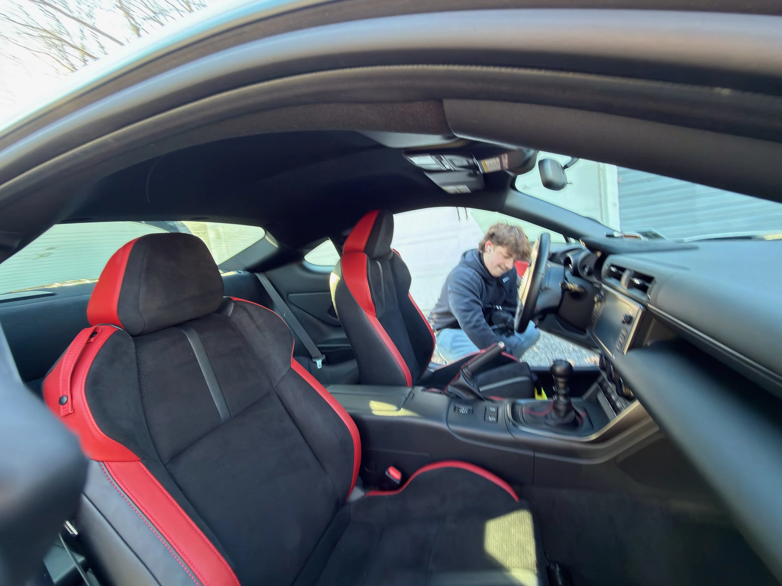 The interior of a car showing a person in the passenger seat and black seats with red accents.
