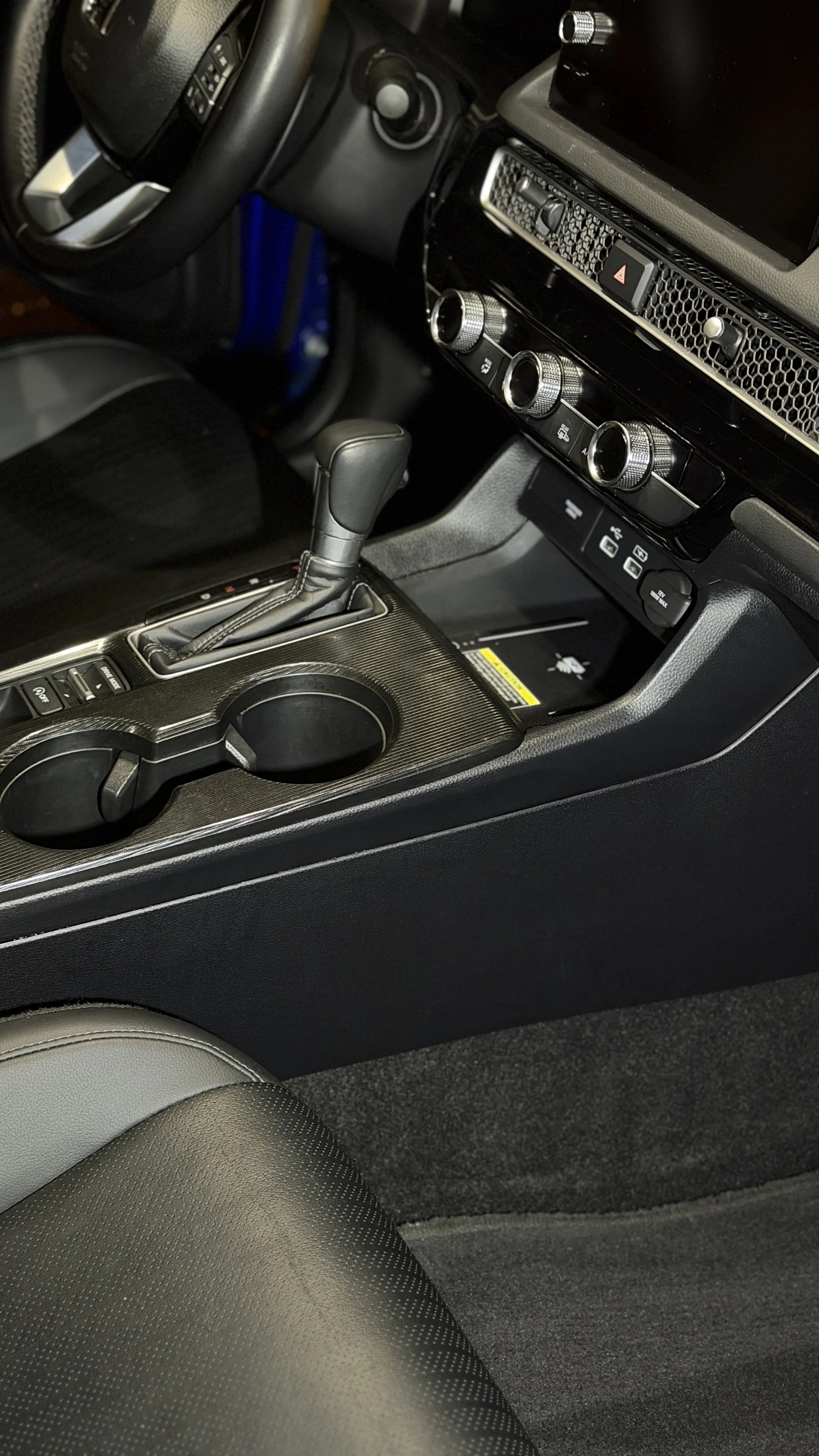 Close-up of a car's center console and gear shift, with climate control knobs and a cup holder visible.
