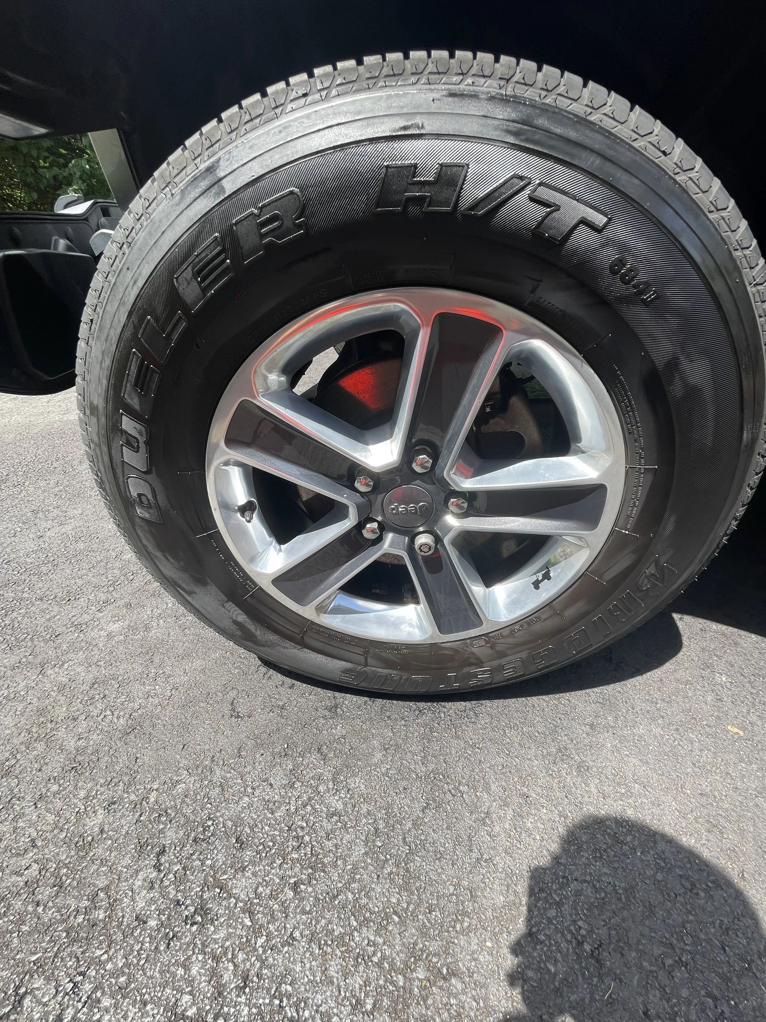 Close-up of a Jeep tire with a black Bridgestone tire and a silver alloy wheel, parked on a paved surface.