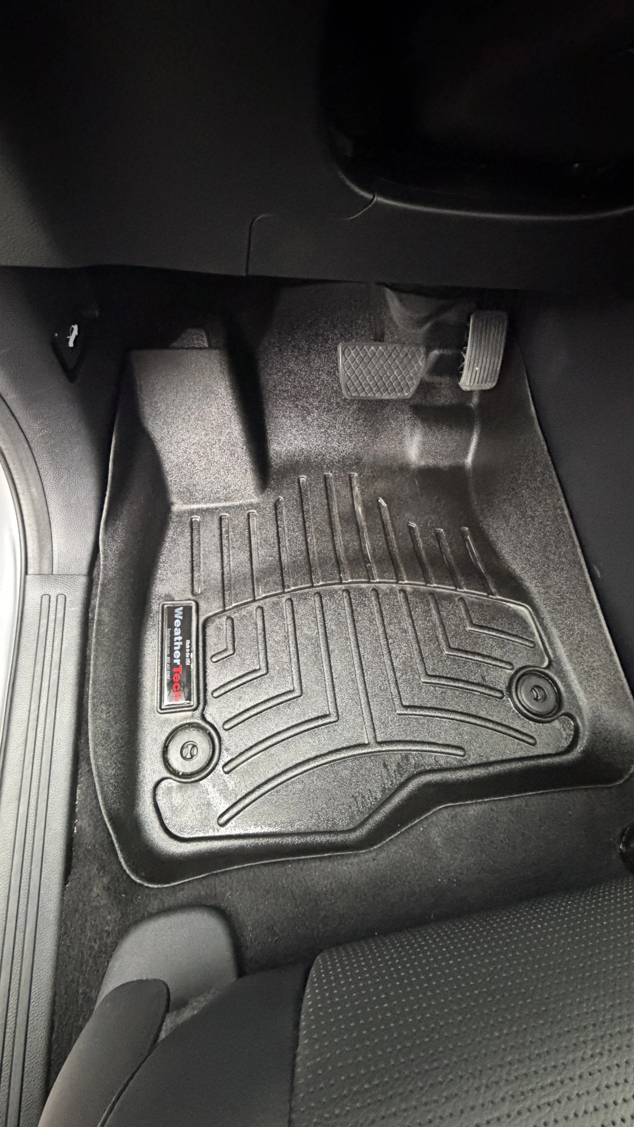 Car floor mat with a WeatherTech brand logo, positioned on the driver's side of a vehicle's interior.