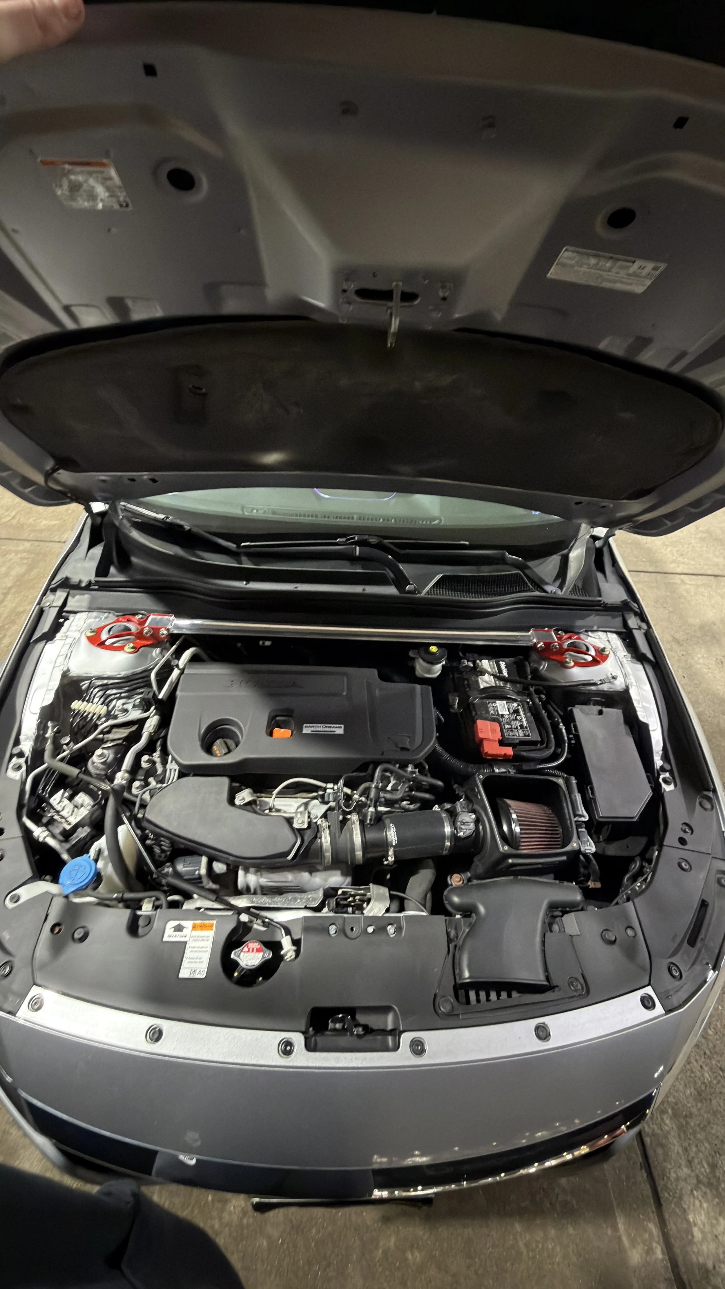 Open car hood showing engine compartment with engine, battery, and various engine components.