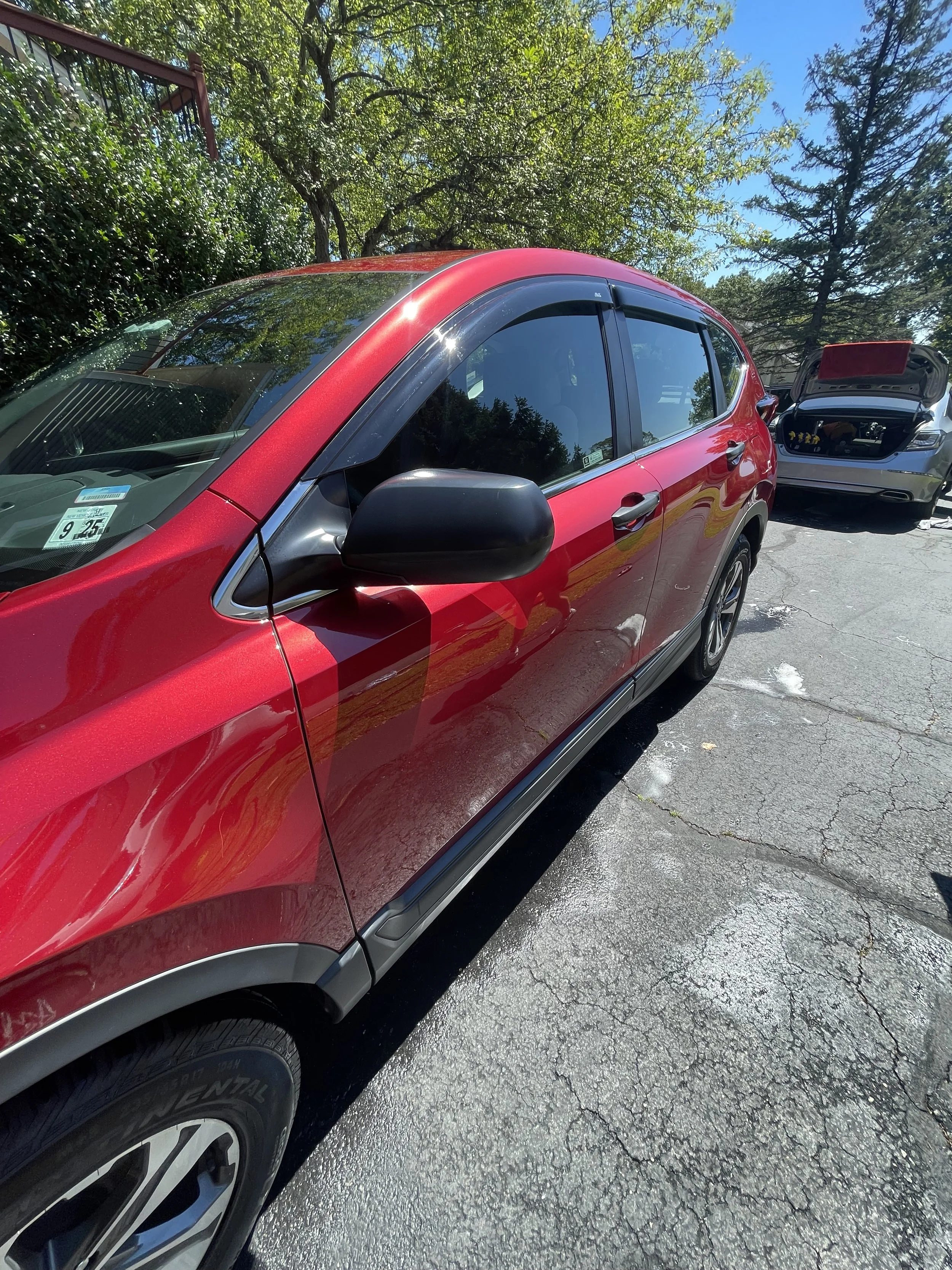 Red SUV parked on a cracked asphalt driveway with trees and blue sky in the background.