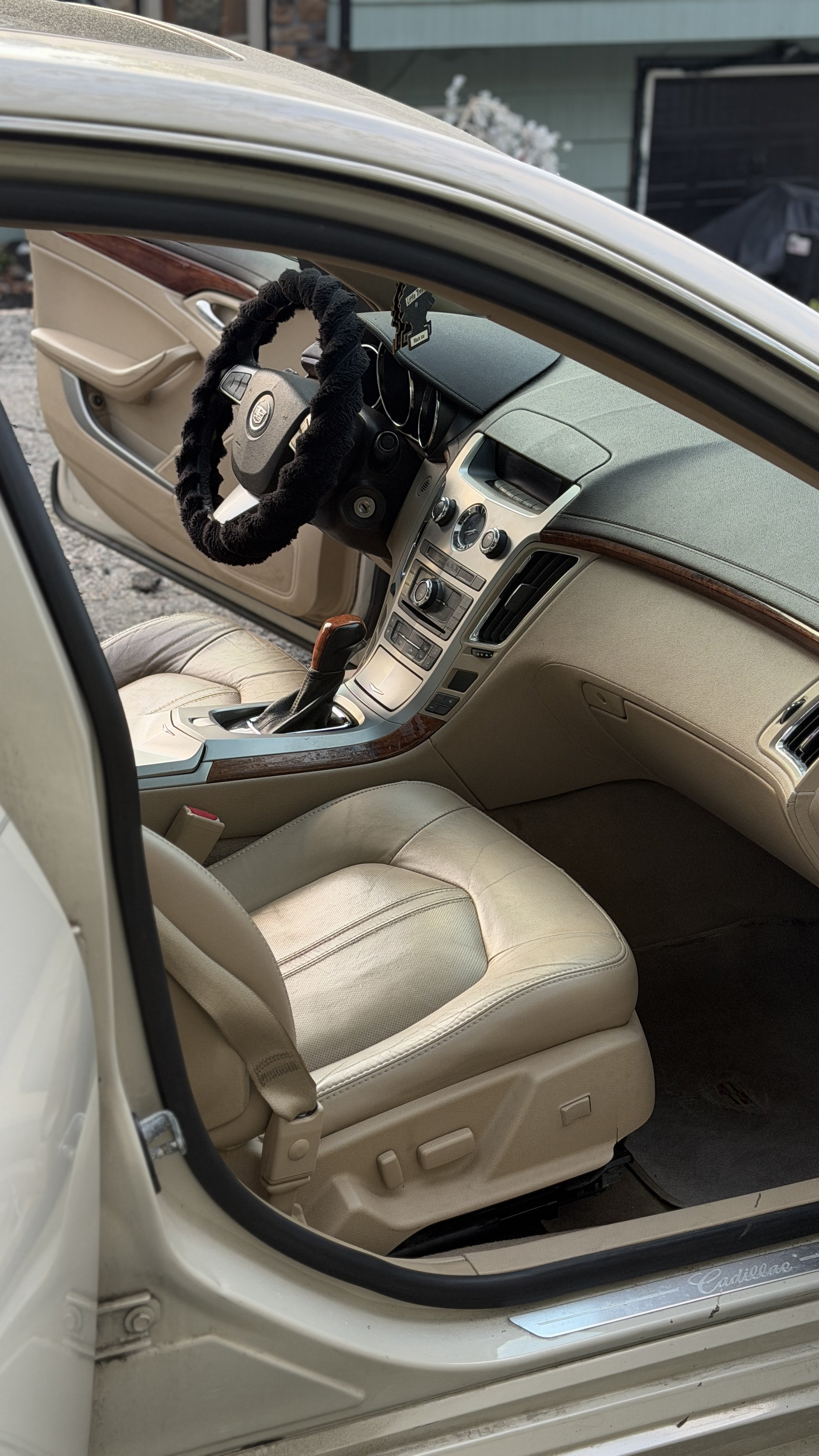 Inside a beige Cadillac car showing the front seats, dashboard, and steering wheel with a black fuzzy cover.