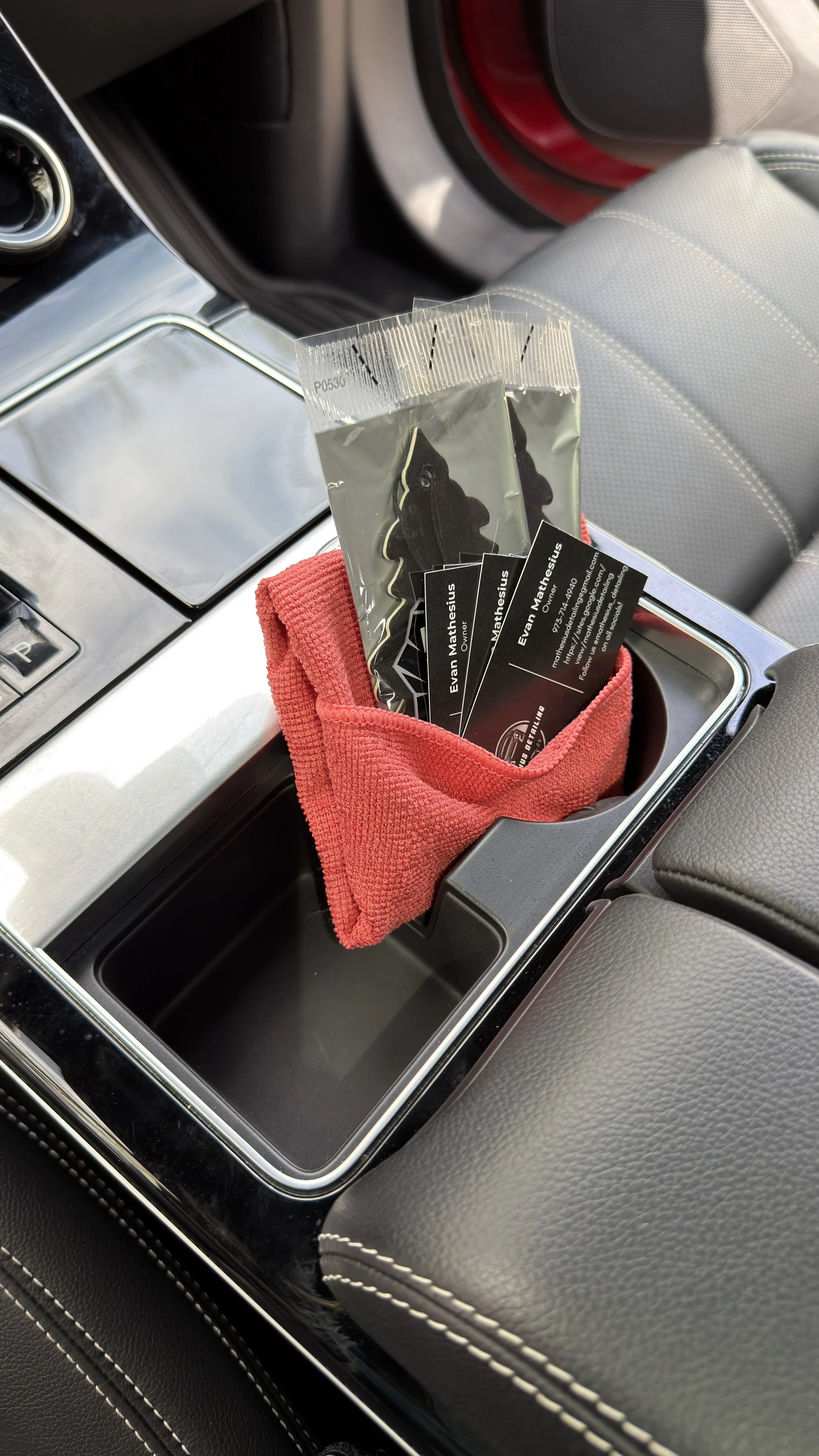 Car's center console with business cards in a red cloth and black plastic bag, and a red towel.