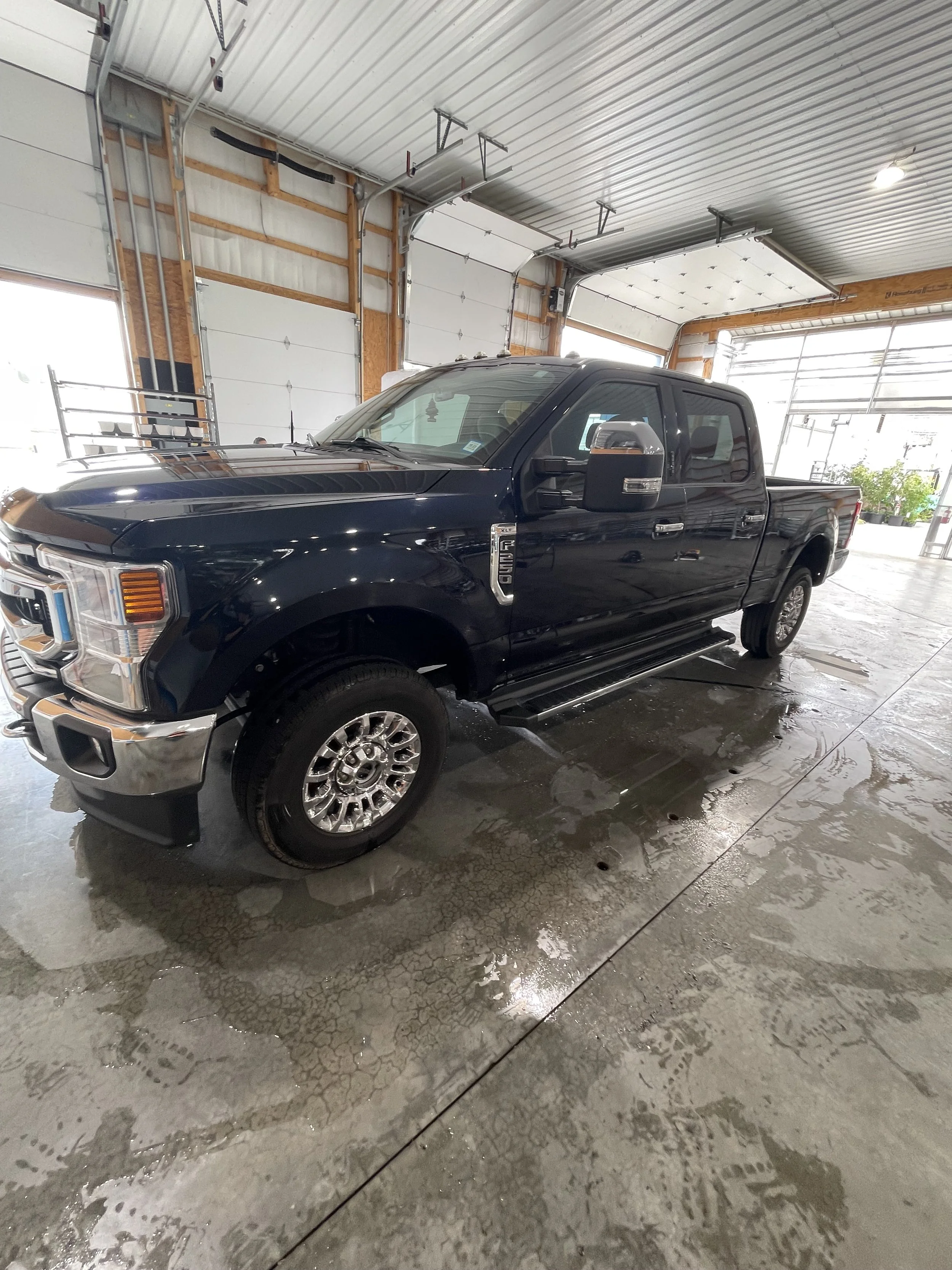 Black pickup truck parked inside a garage with a concrete floor and metal ceiling, with some water on the ground.
