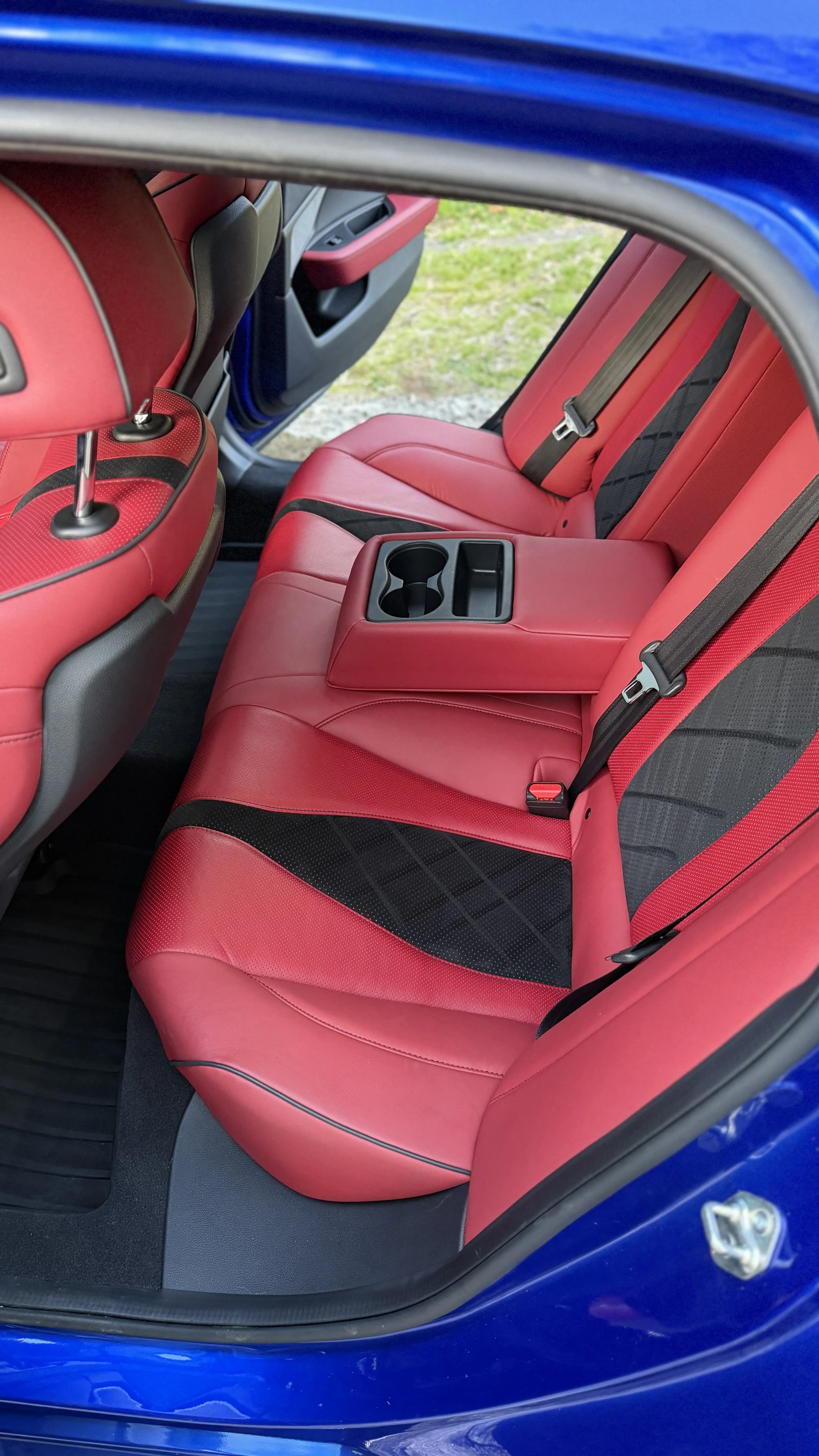 Red leather back seats of a blue car with a fold-down armrest with cup holders.