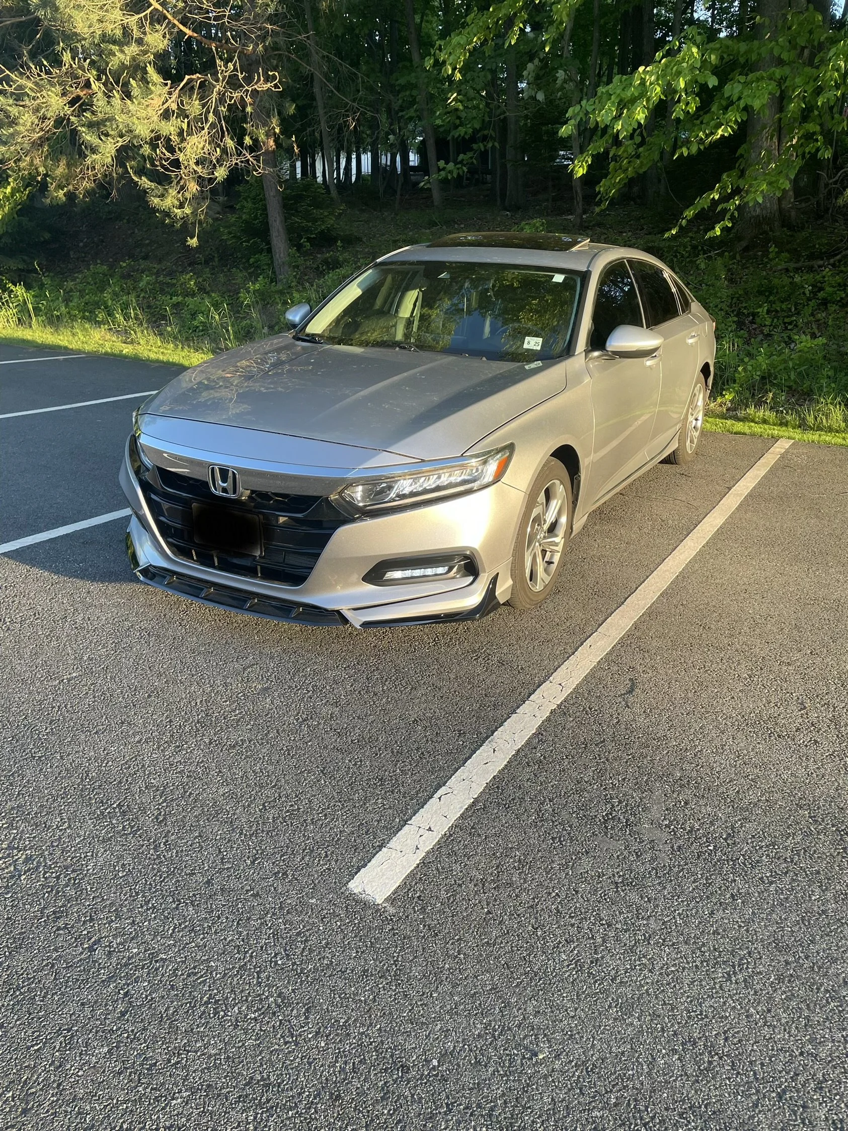 A silver Honda Civic parked in a parking lot with white lines, next to a grassy area and a wooded background.