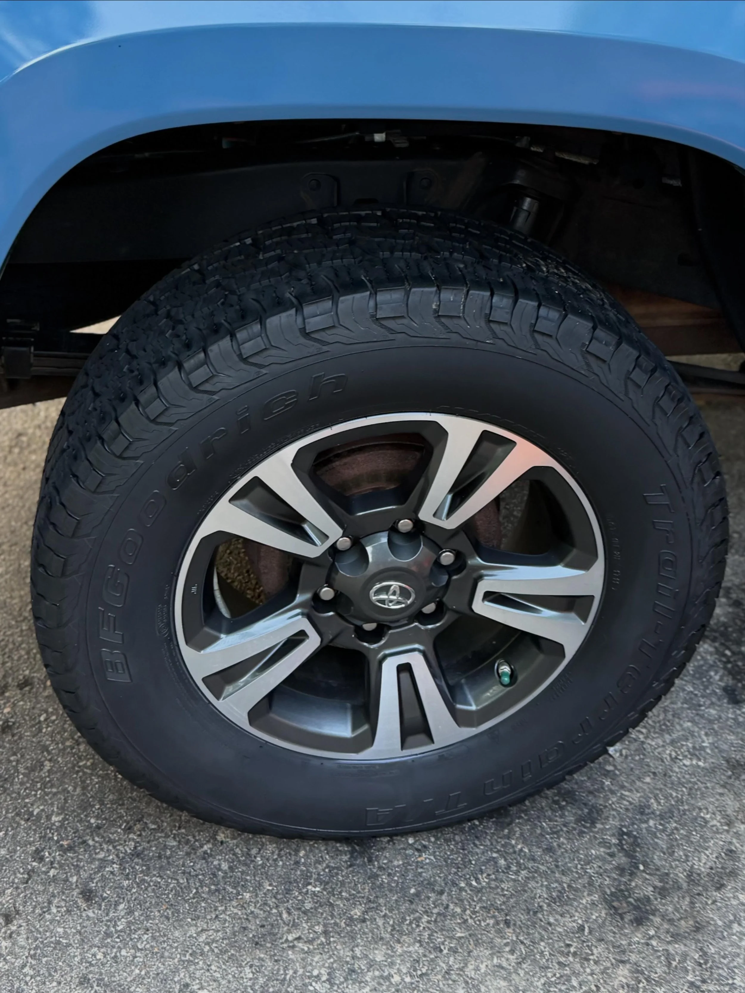 Close-up of a car tire mounted on a rim, with a blue vehicle body above it and pavement below.