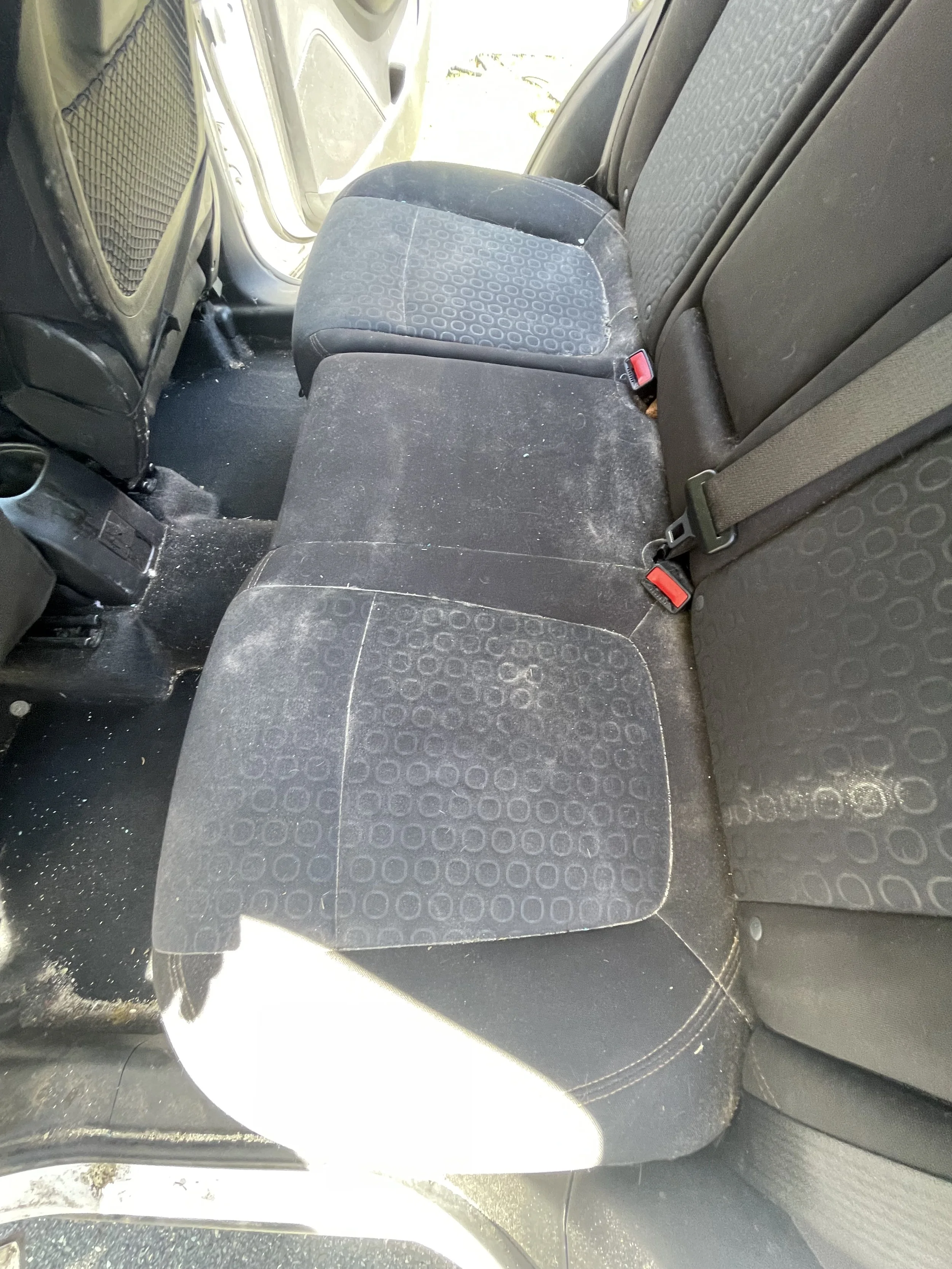The back seat of a vehicle, with two cloth seats, the middle seat is folded down. There is dirt and debris on the seats and floor.