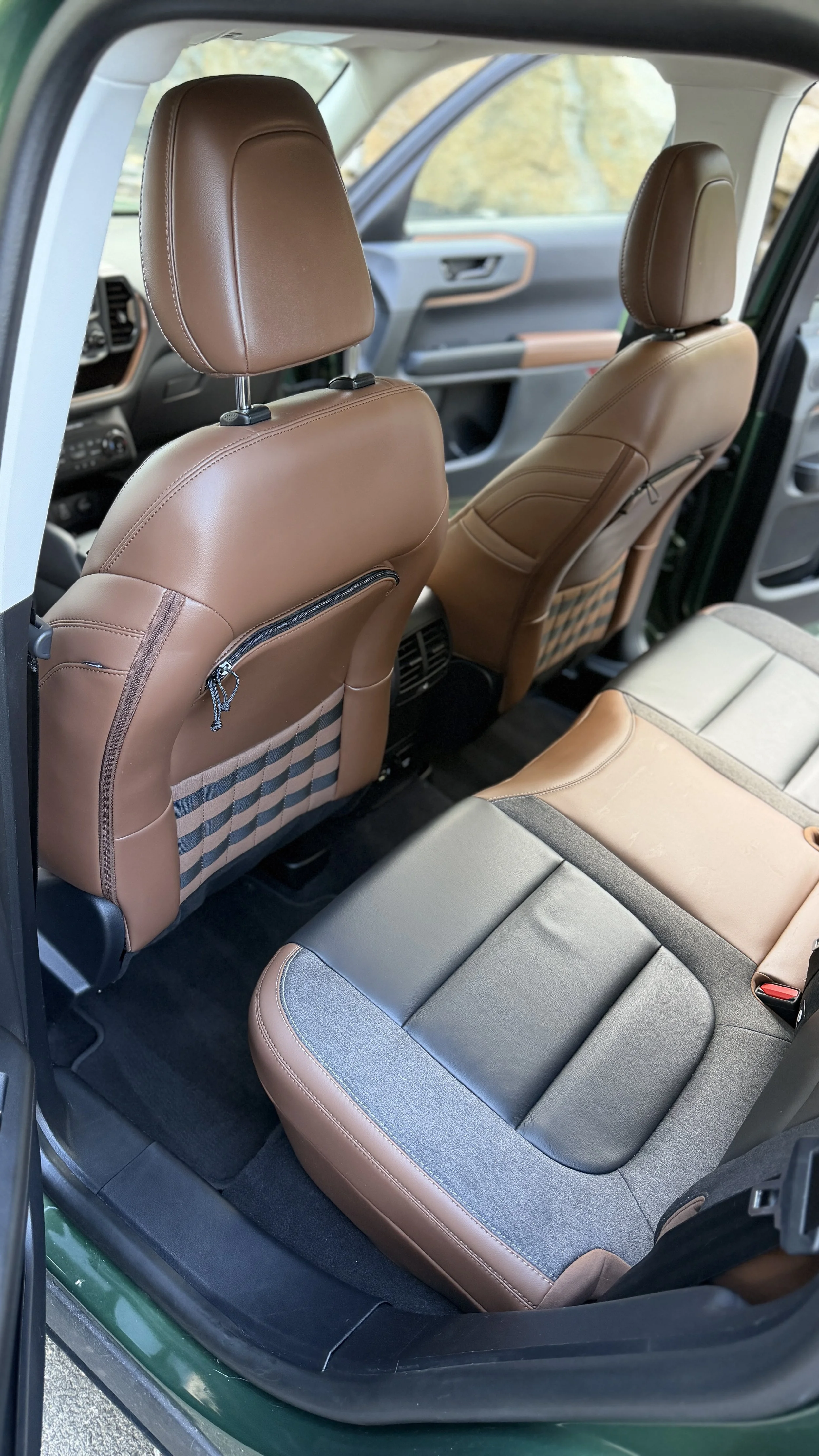 Interior of a car showing tan leather front seats, rear seat with gray and tan upholstery, and the dashboard visible through the windshield.
