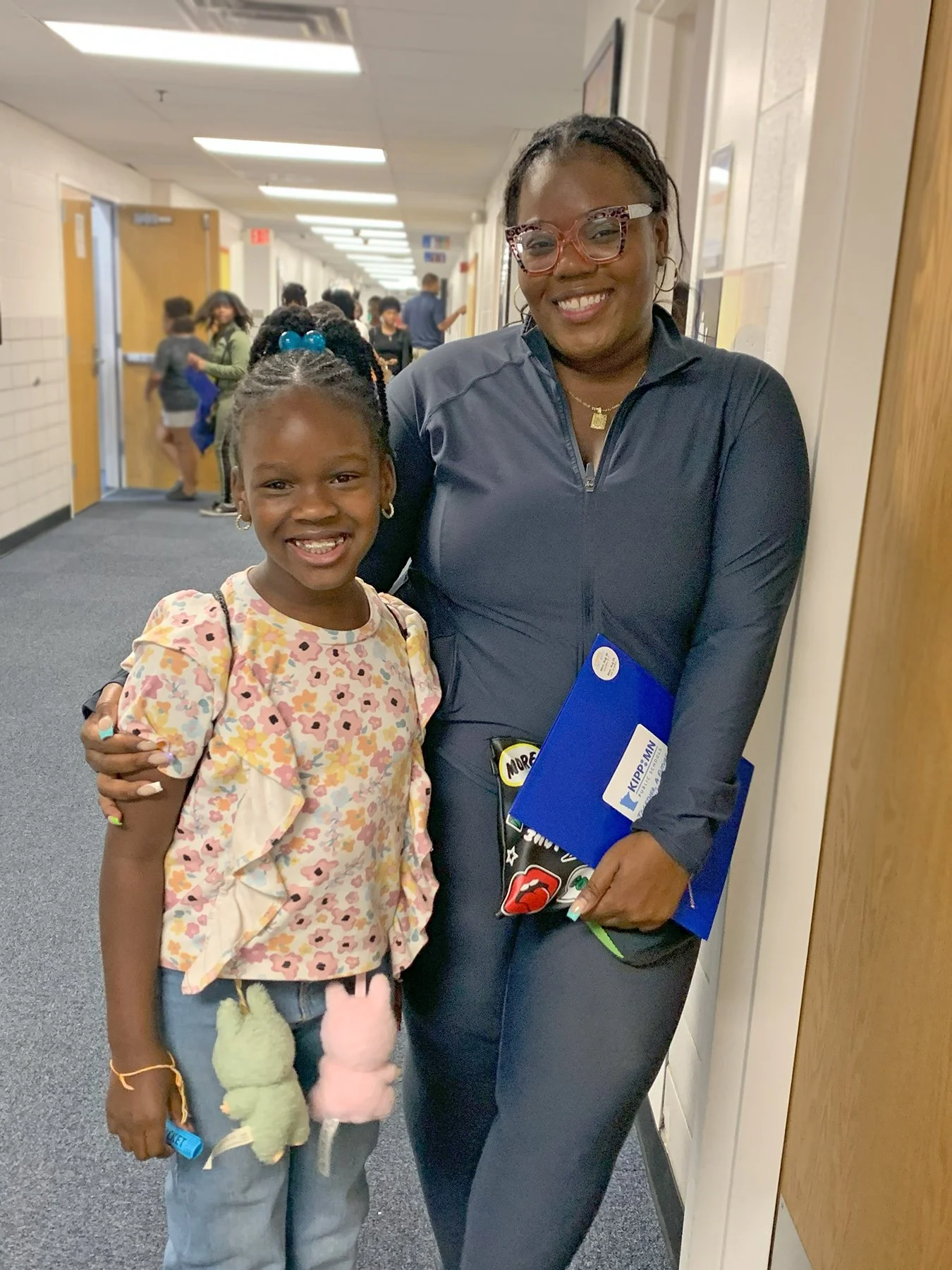 A woman and girl smiling and hugging in a school hallway.