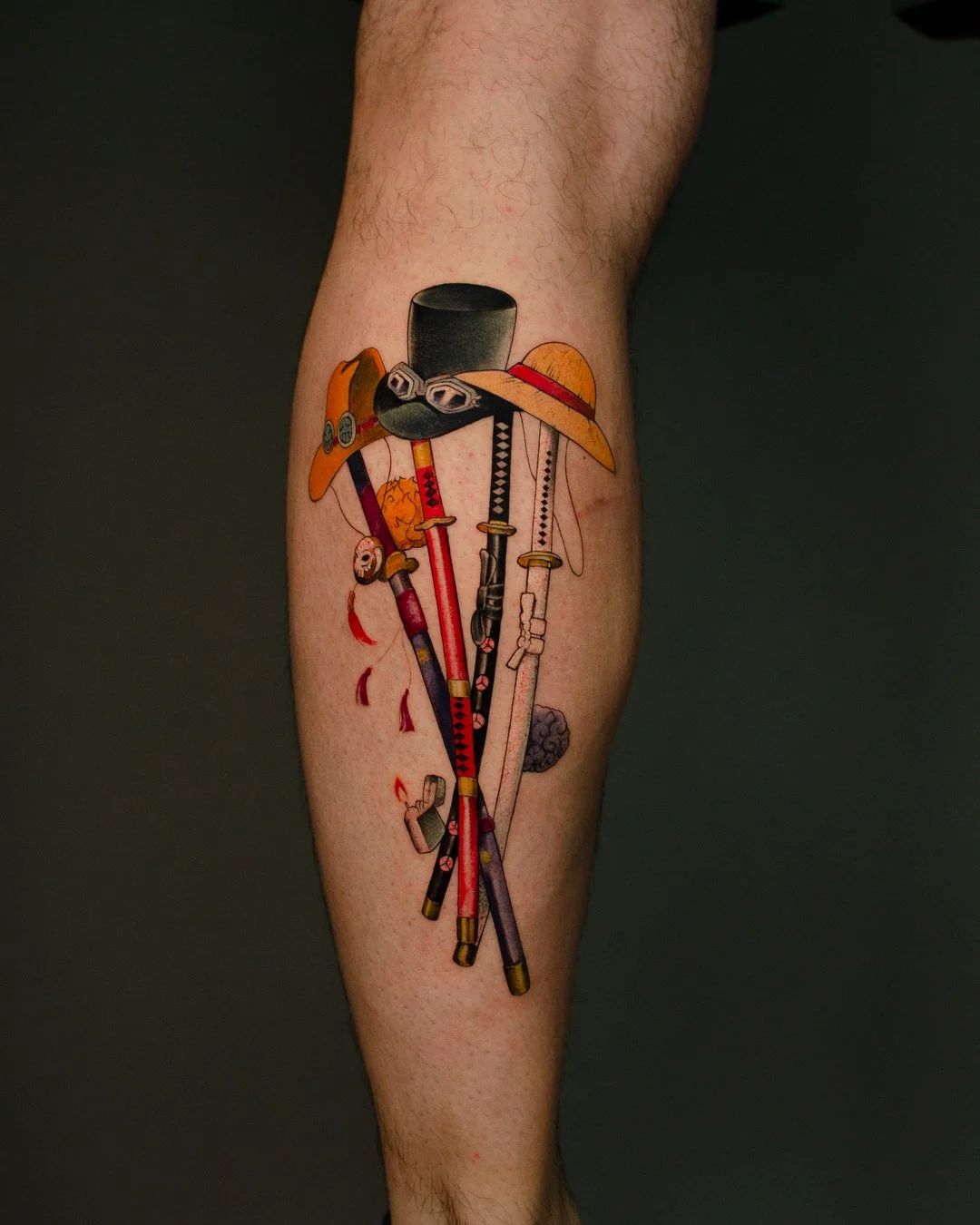 Colorful tattoo of four different swords with hats and accessories on a person's lower leg.