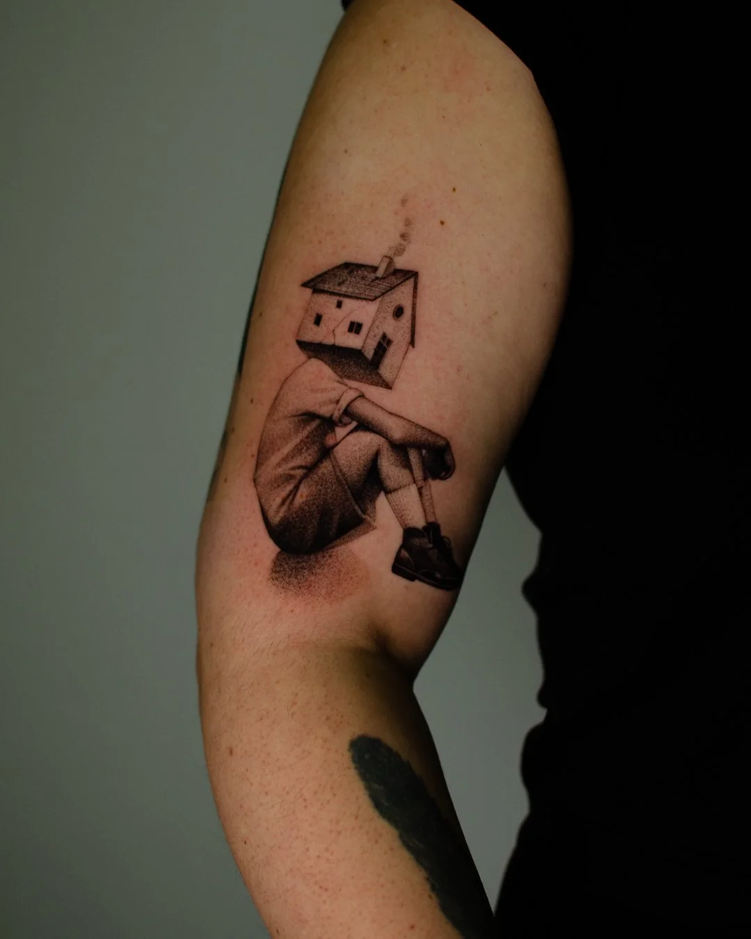 Tattoo of a person with a house for a head, smoking a cigarette and resting their chin on their knee.