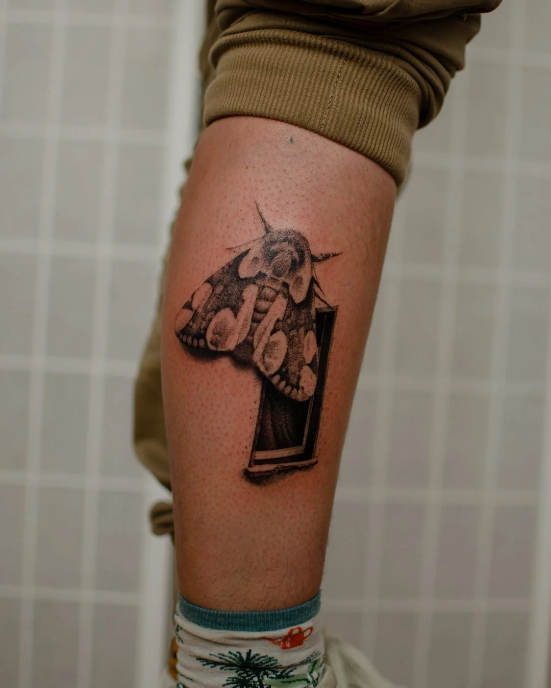 A tattoo of a moth on a person's thigh, with the moth partially over a rectangular shape.