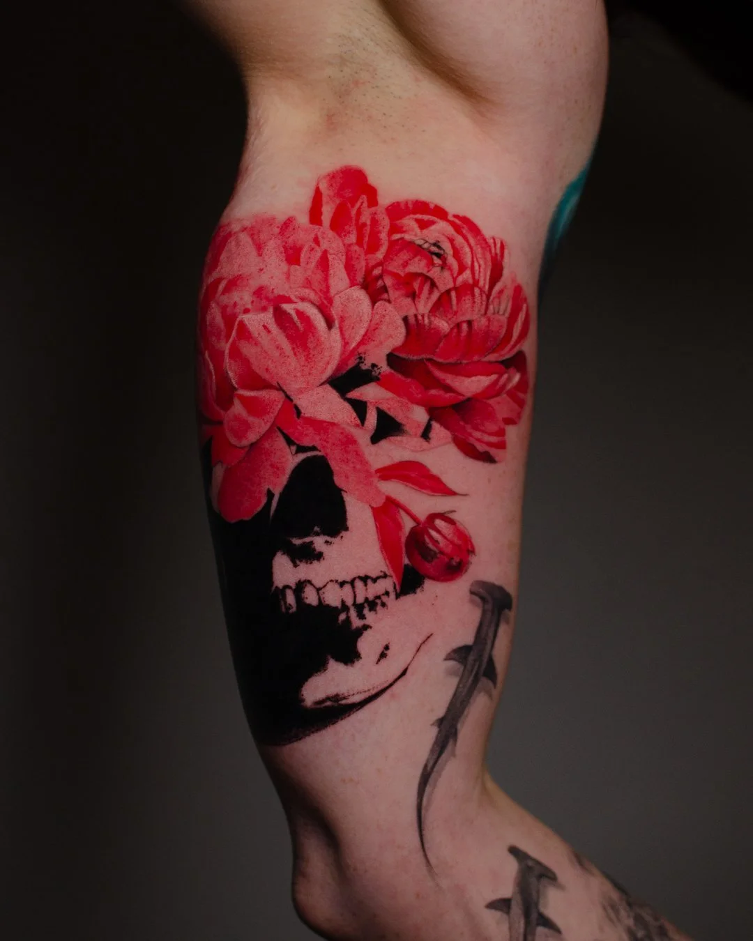 Tattoo of a pink flower, a skull, and a dagger on a person's arm.