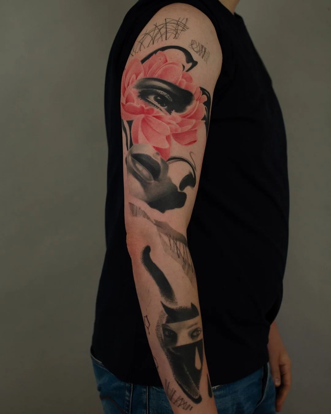 Tattoo of a woman's face with an eye and full lips, surrounded by a pink flower, and a face covered with a mask with eyes showing, on a person's arm.