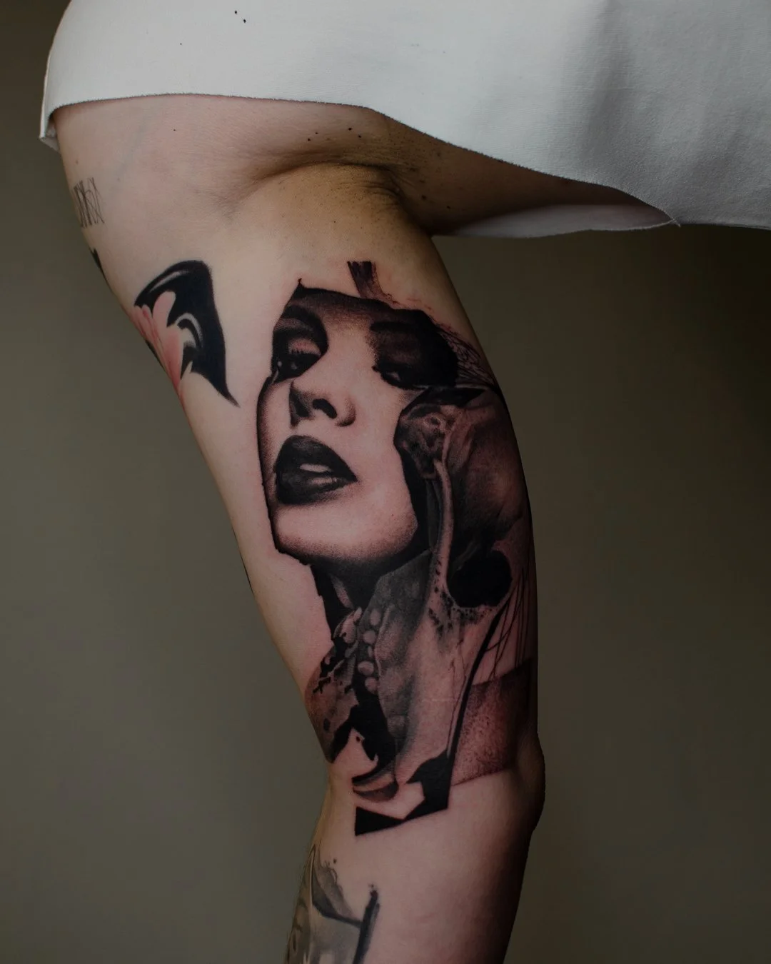 Tattoo of a woman's face with dark lipstick and eyeshadow, and additional abstract and skull elements on a person's thigh.