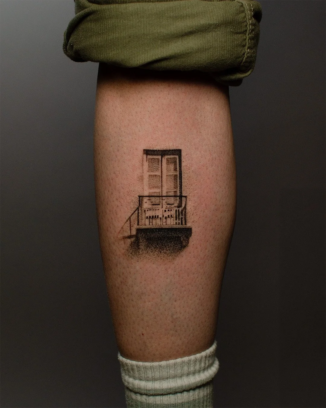 Tattoo of a balcony with a door and window on a person's thigh.