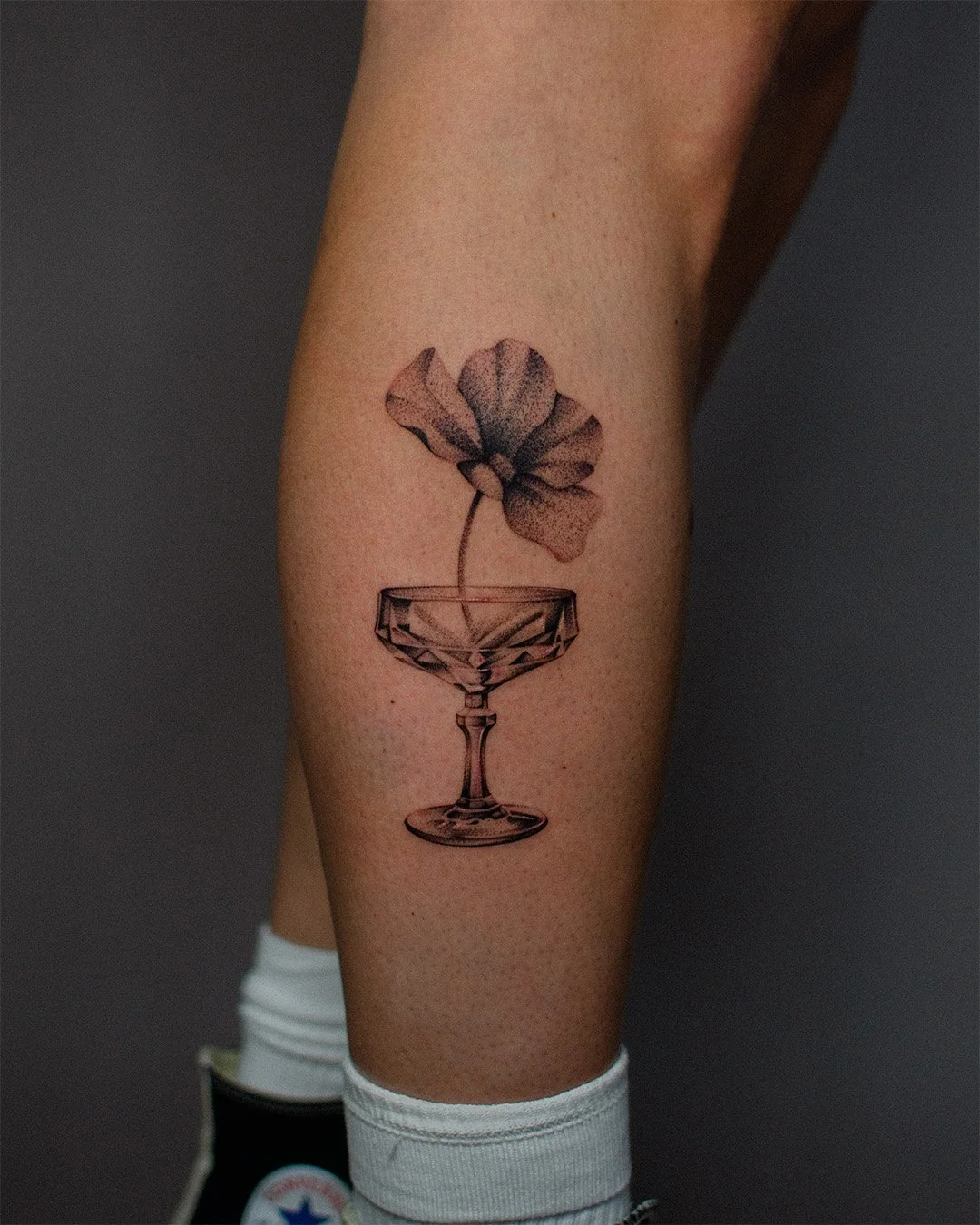 Tattoo of a flower in a cocktail glass on person's leg.