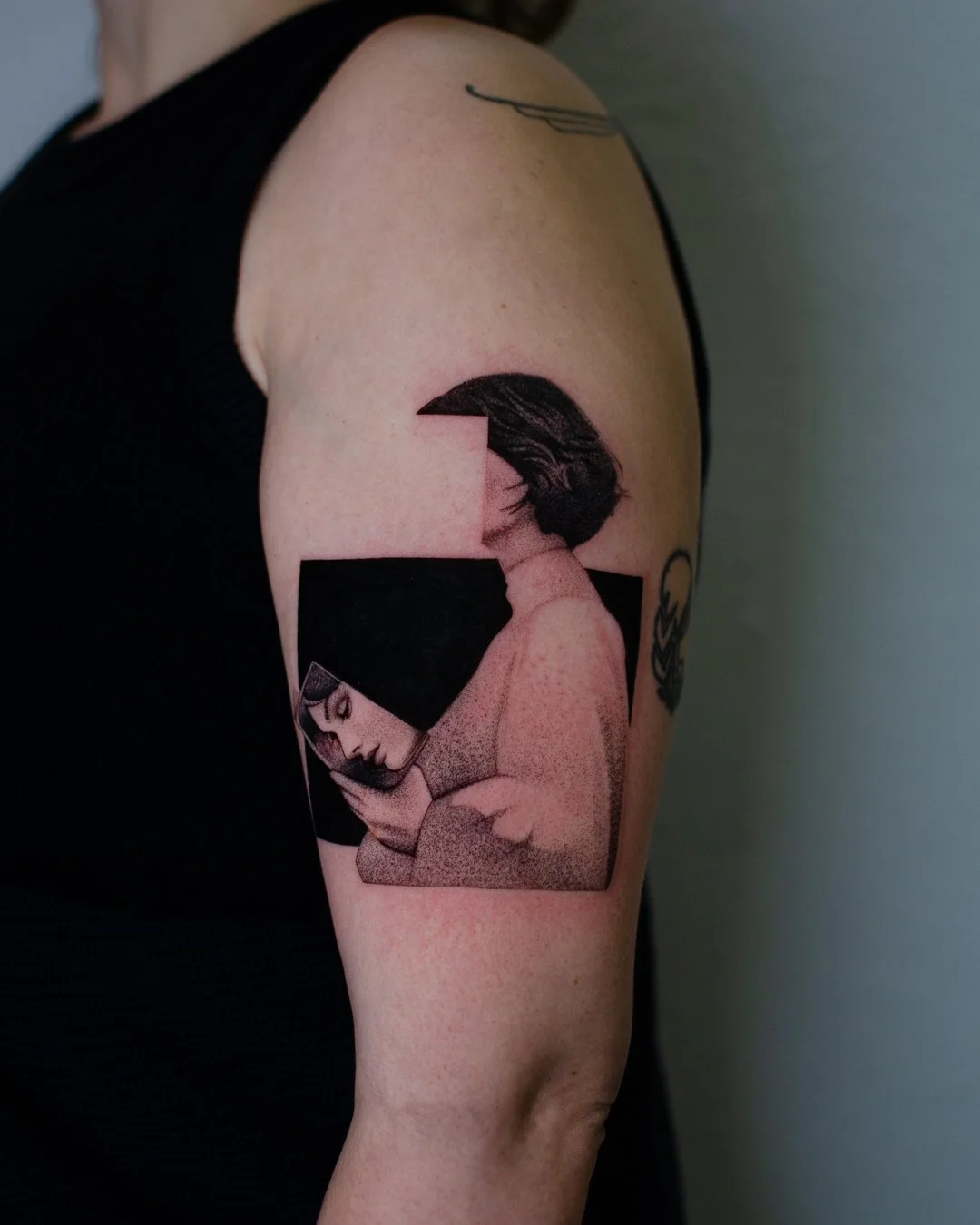 Tattoo of a woman with dark hair looking at a phone, in a style combining dot work and shading, with geometric shapes around her, on an upper arm.