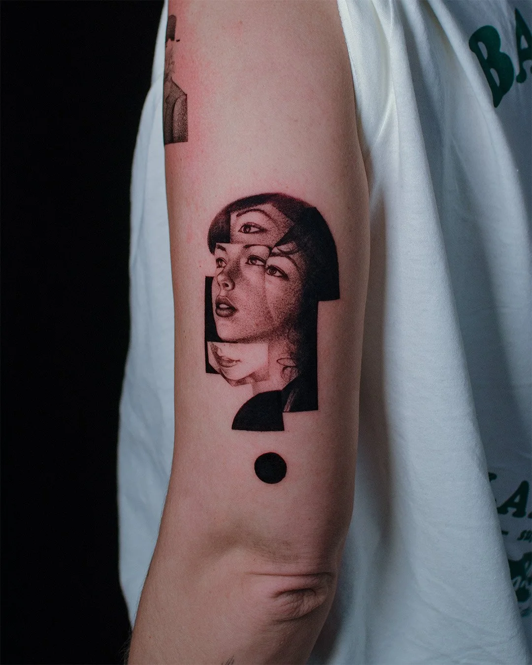 Tattoo of a woman's face with multiple layered and fragmented facial features and a black dot below on a person's upper arm.