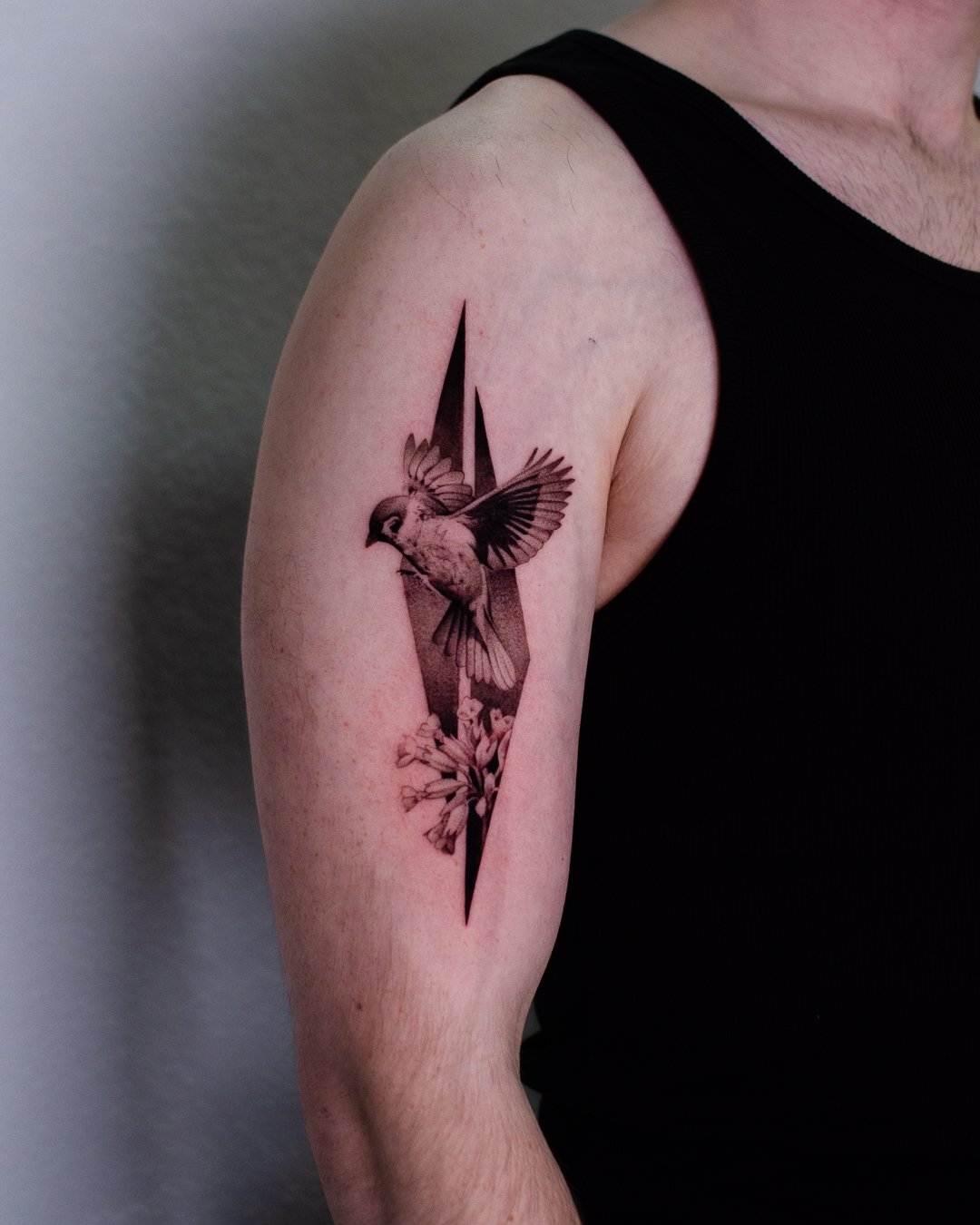 Tattoo of a bird in flight with open wings, surrounded by flowers, and a vertical split in the background on a person's upper arm.