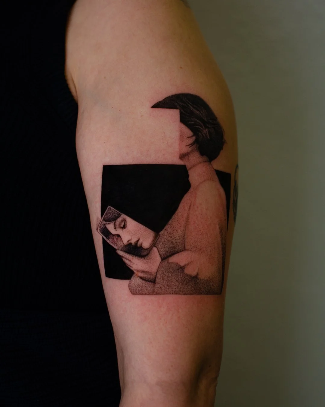 Tattoo of a woman with short hair looking at a photograph of herself with closed eyes on upper arm.