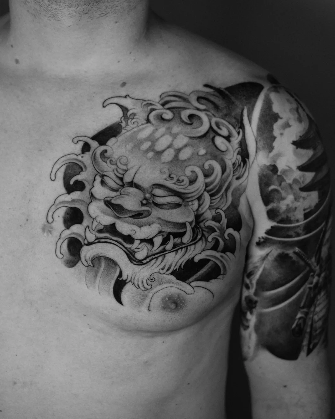 Close-up of a black and white tattoo on a person's shoulder, featuring a stylized dragon with swirling clouds.