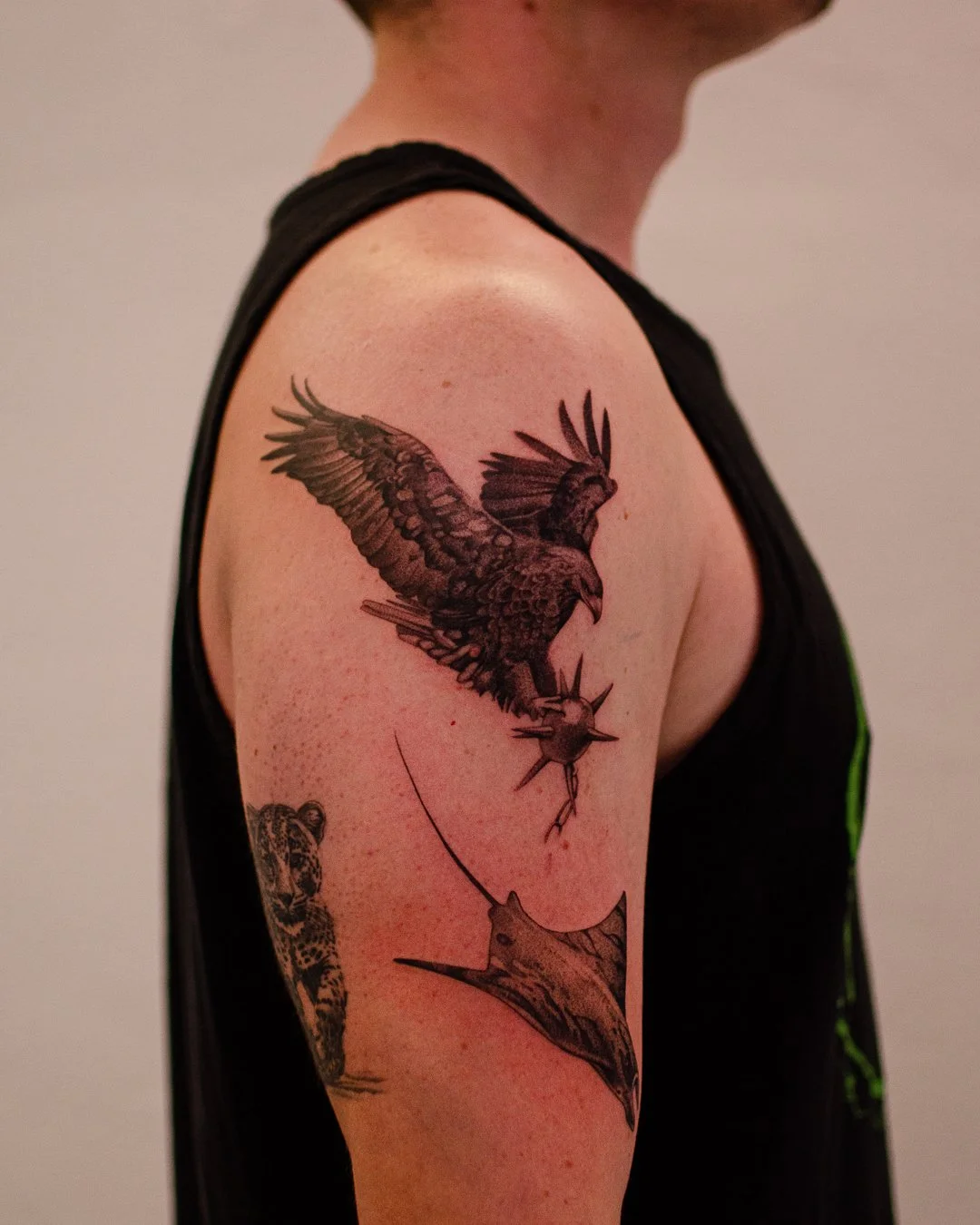 Tattoo of a bird of prey grabbing a fish with a stingray underneath on the upper arm of a person wearing a black tank top.