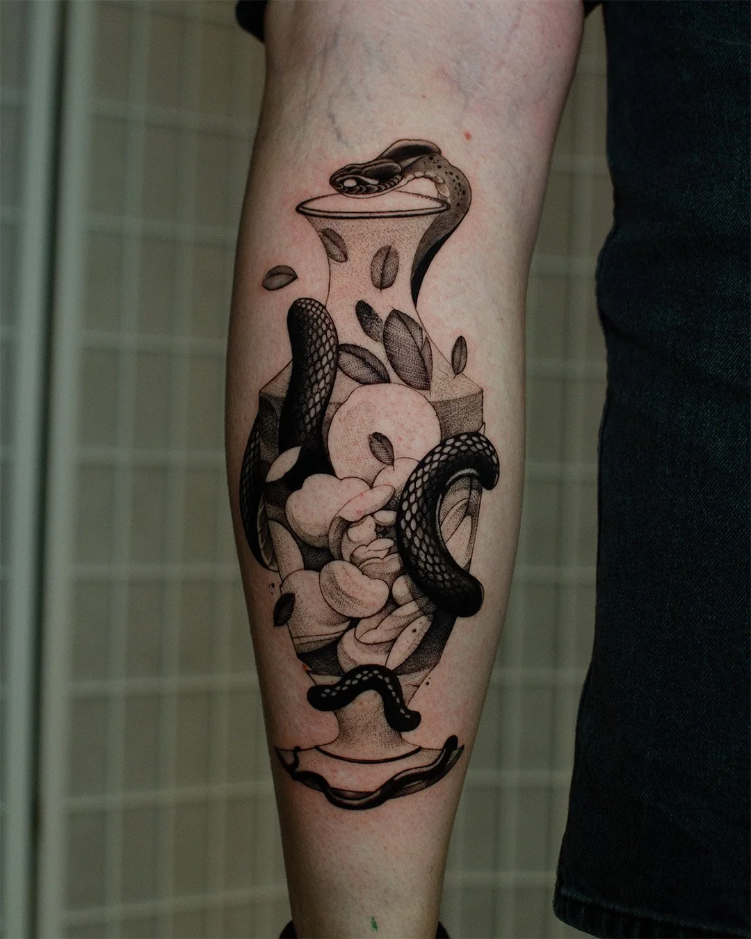 Black and grey tattoo of a snake, coffee beans, and leaves inside a large glass coffee pot on a person's lower leg.