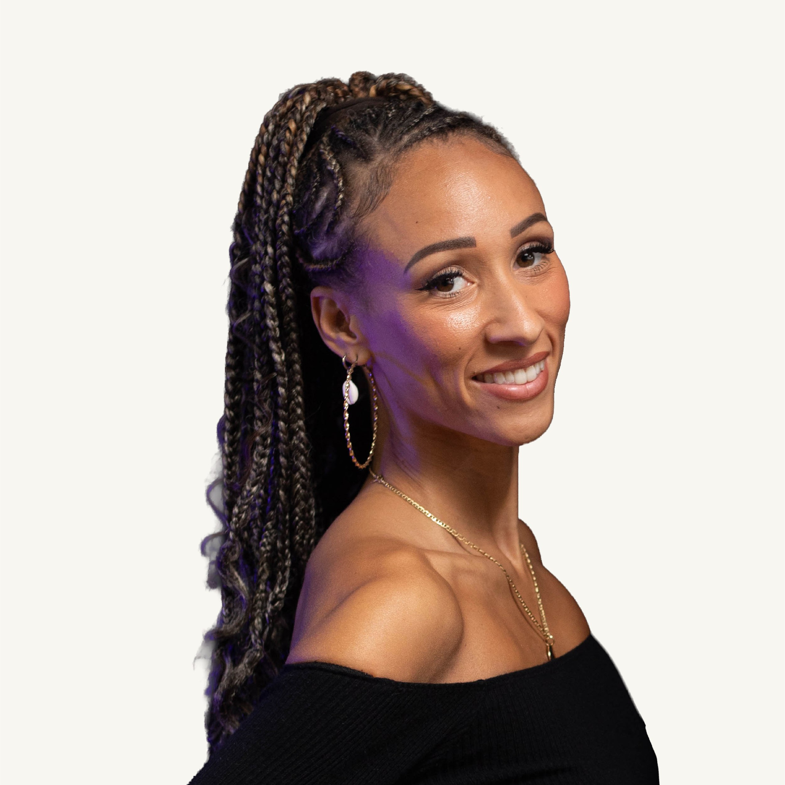 Un portrait d'une femme souriante avec des cheveux tressés et un maquillage subtil, portant des bijoux en or, sur fond blanc.