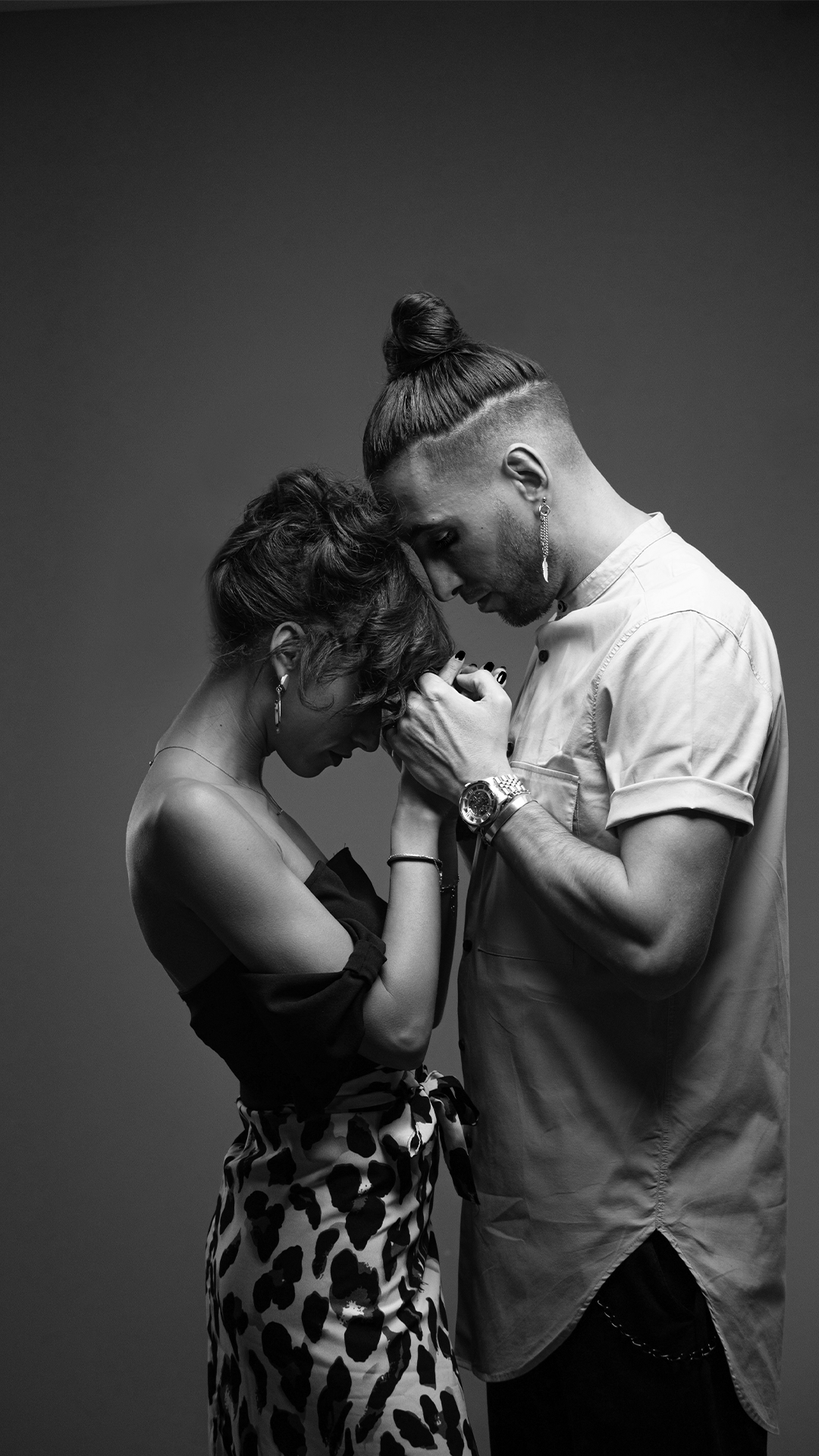 Un couple en noir et blanc se tient la tête penchée, mains jointes et yeux fermés, exprimant une émotion profonde.