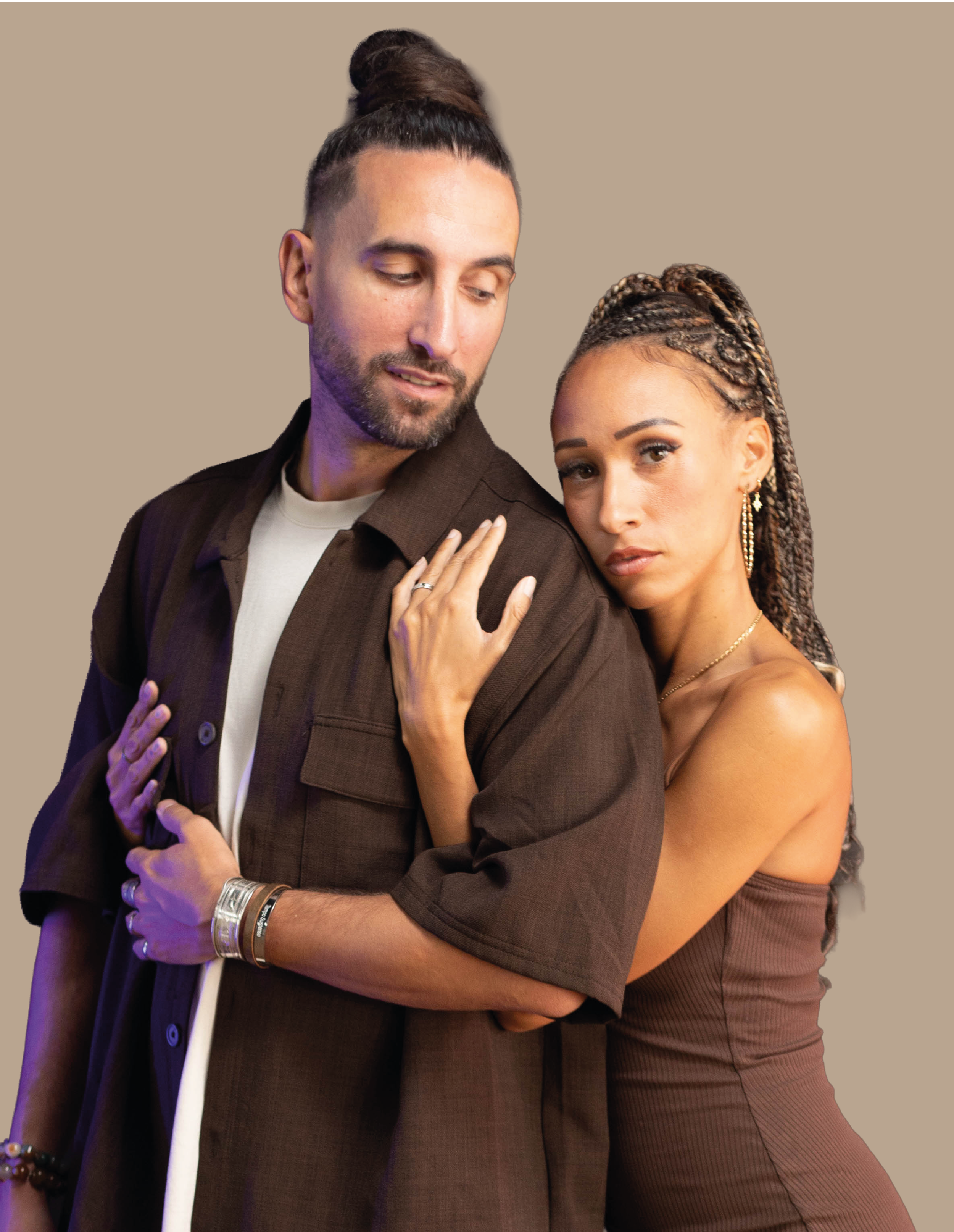 Deux personnes, un homme et une femme, posent étroitement l'un contre l'autre, la femme touche l'épaule de l'homme, tous deux regardent légèrement vers le bas, avec un fond neutre beige.