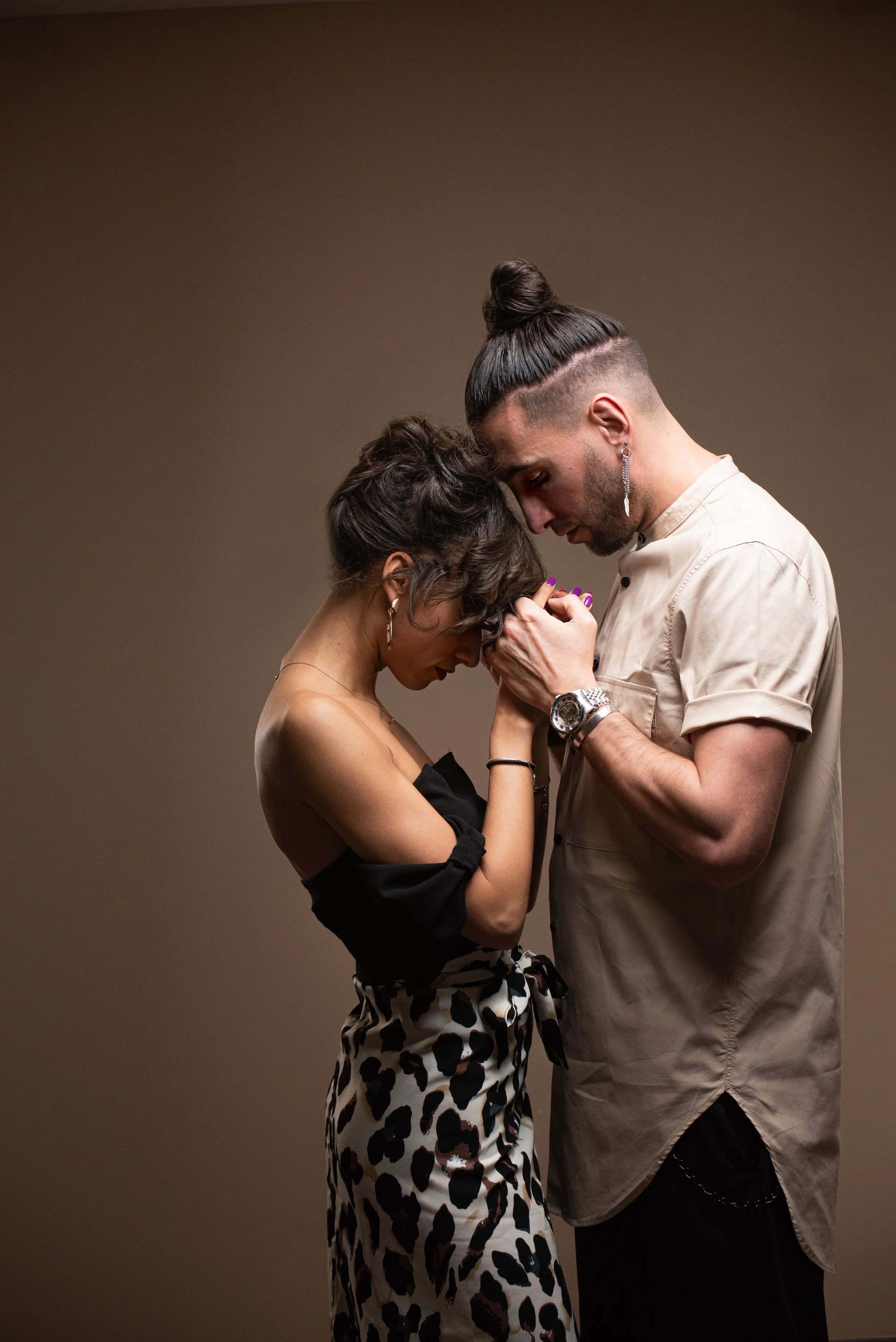 Un homme et une femme se tiennent très proches, la tête appuyée l'un contre l'autre, dans une posture intime et émotive, avec un fond neutre.