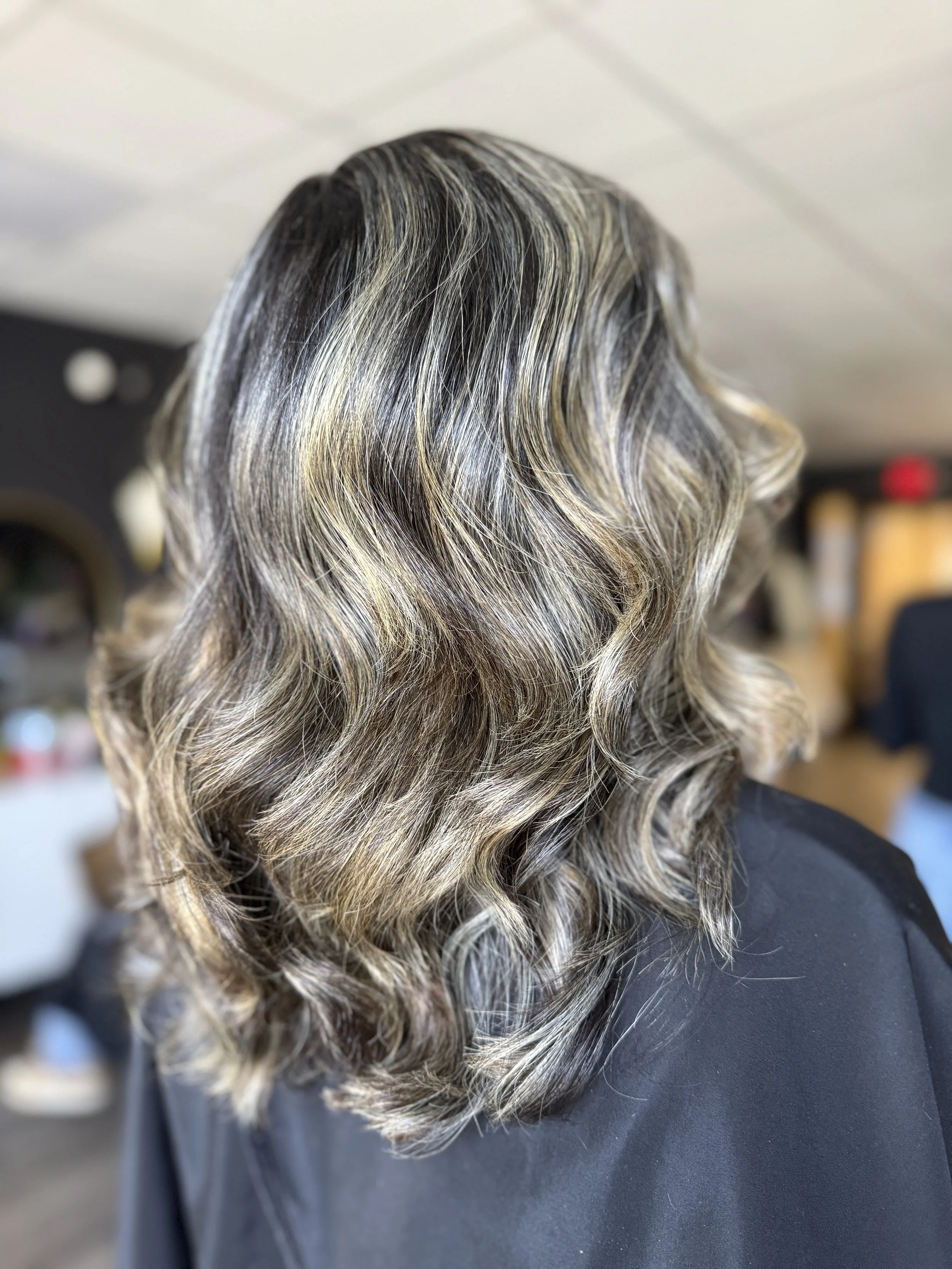 Woman's wavy, shoulder-length blonde hair with dark roots and highlights.