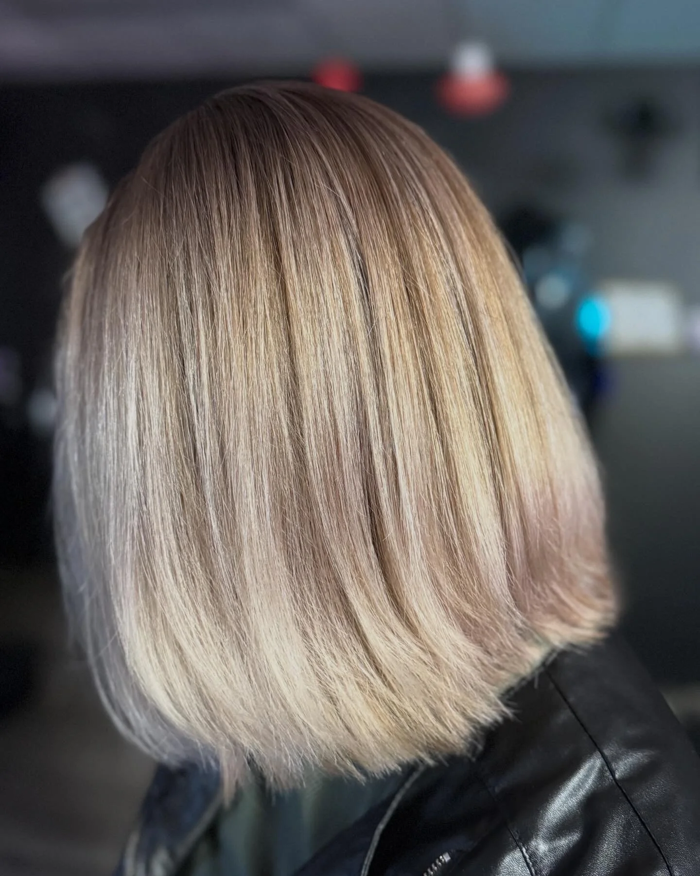 Close-up of a person's hair in a bob cut with blonde color and subtle pink tones, shot from the side with a dark background.