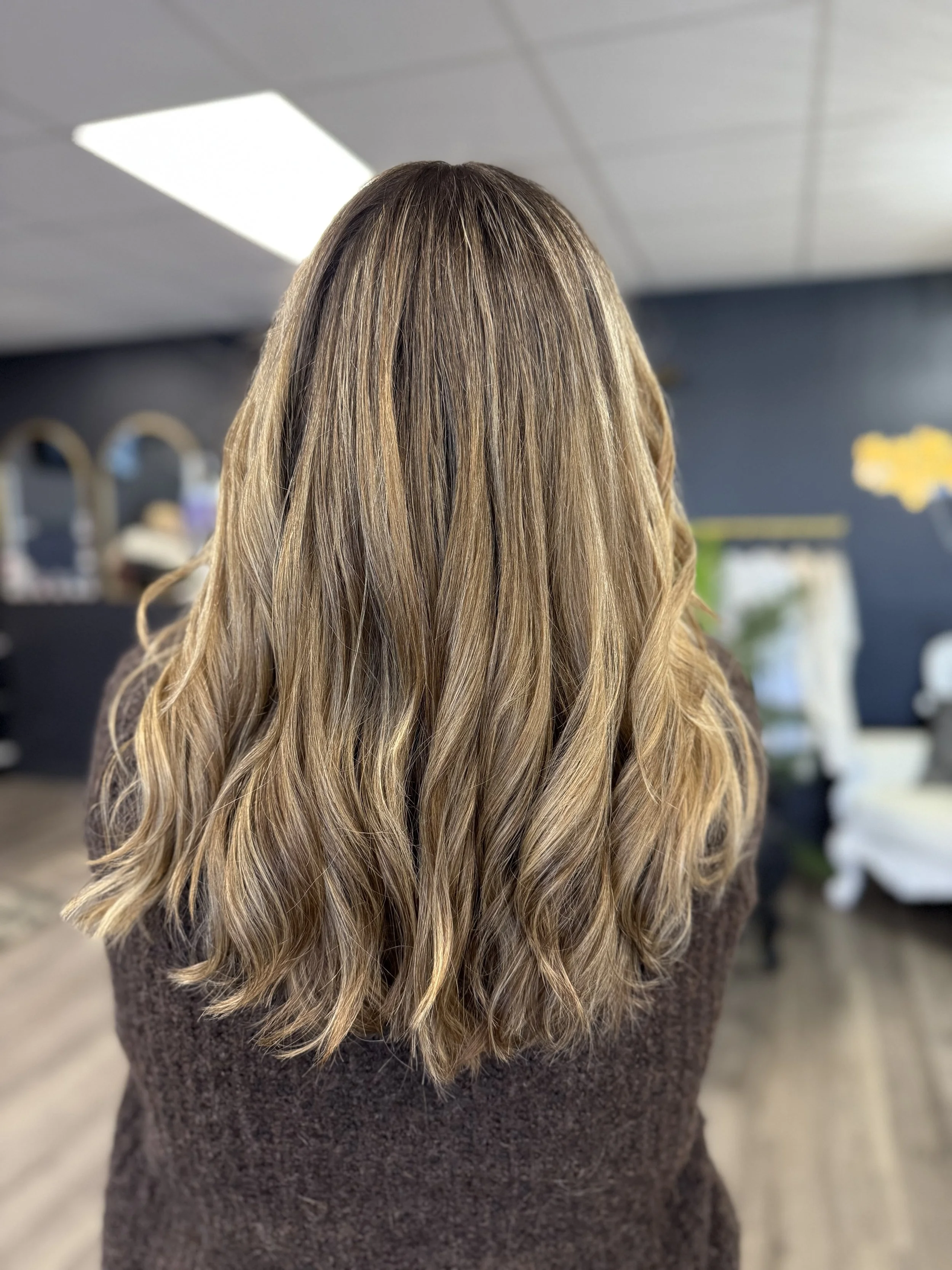 Back of a woman with long, wavy, blonde hair in an indoor setting.