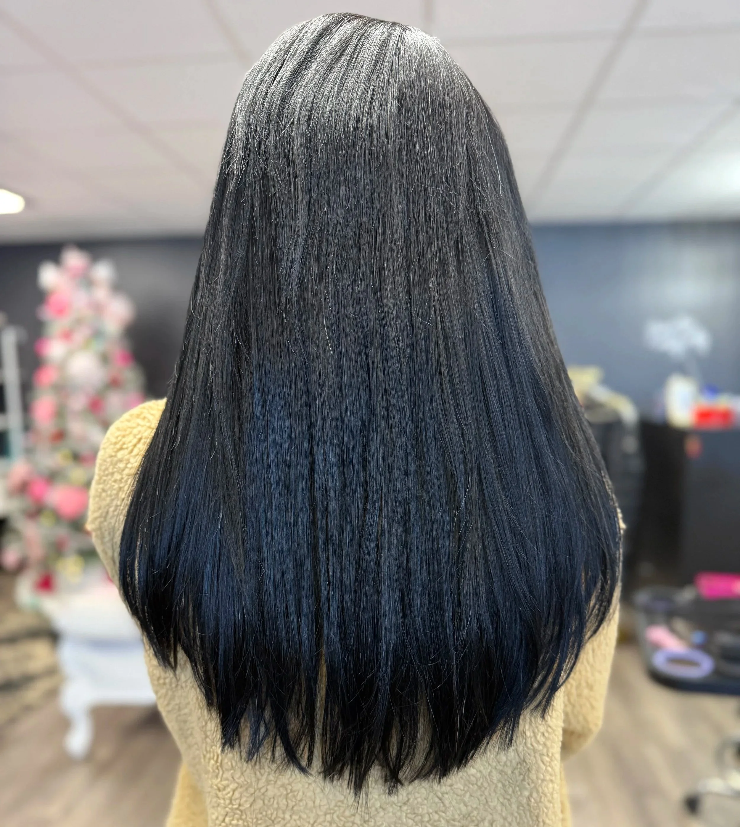 Back view of a woman with long, straight black hair in an indoor setting.