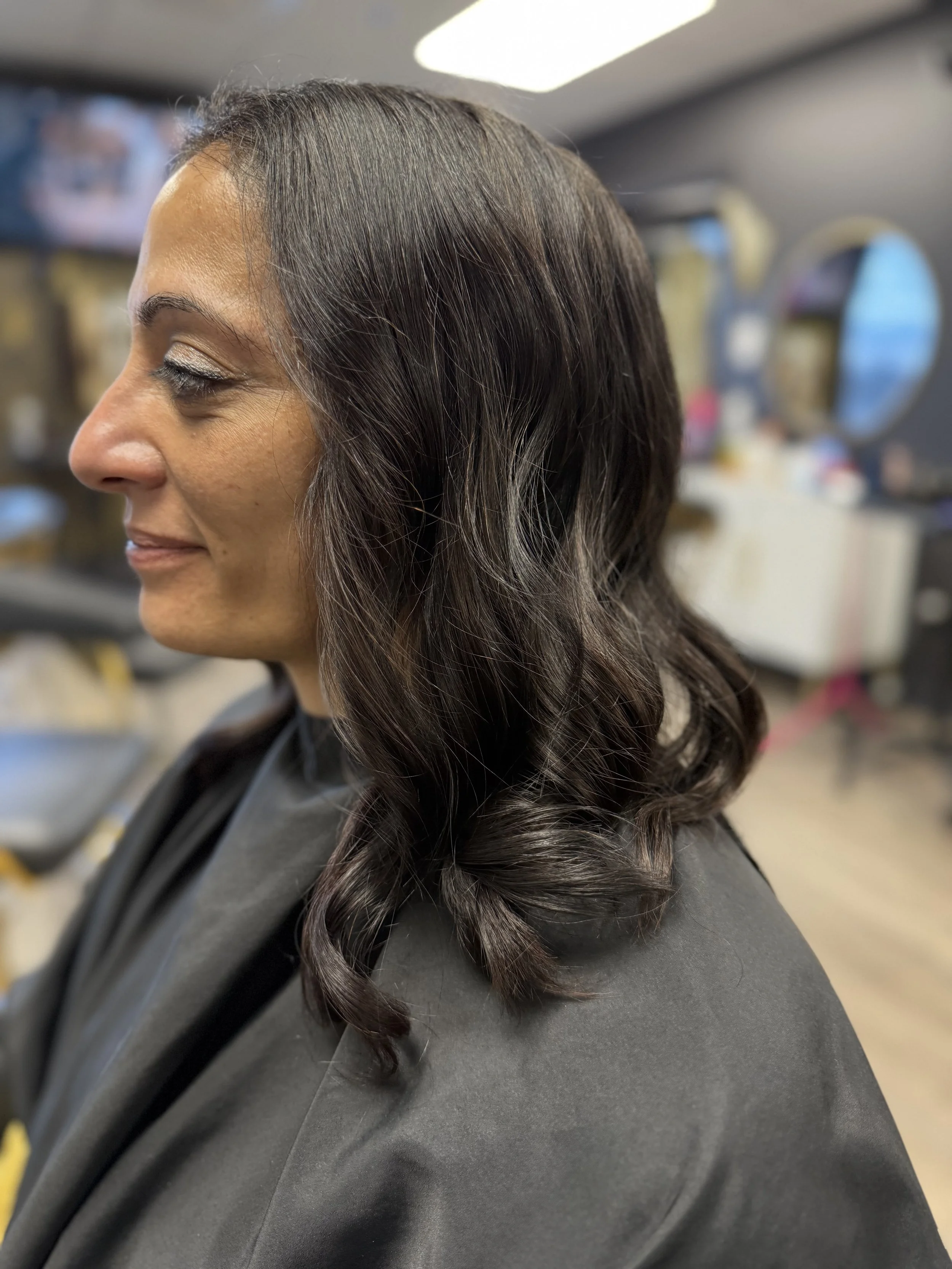 Side view of woman with shoulder-length dark brown wavy hair at a salon.