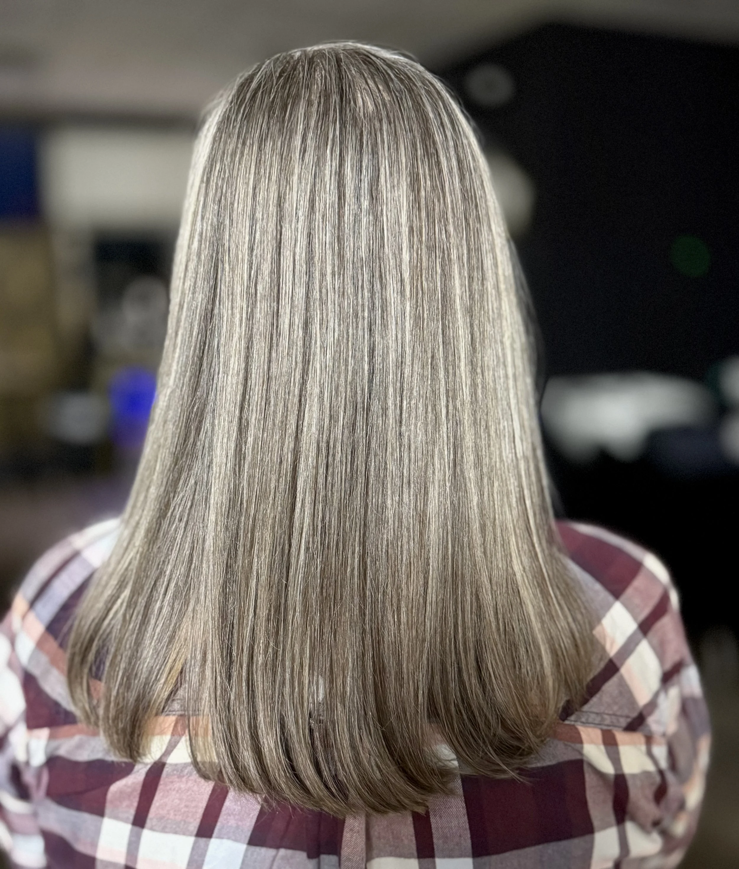 Back view of a woman with straight, shoulder-length blonde hair wearing a plaid shirt.