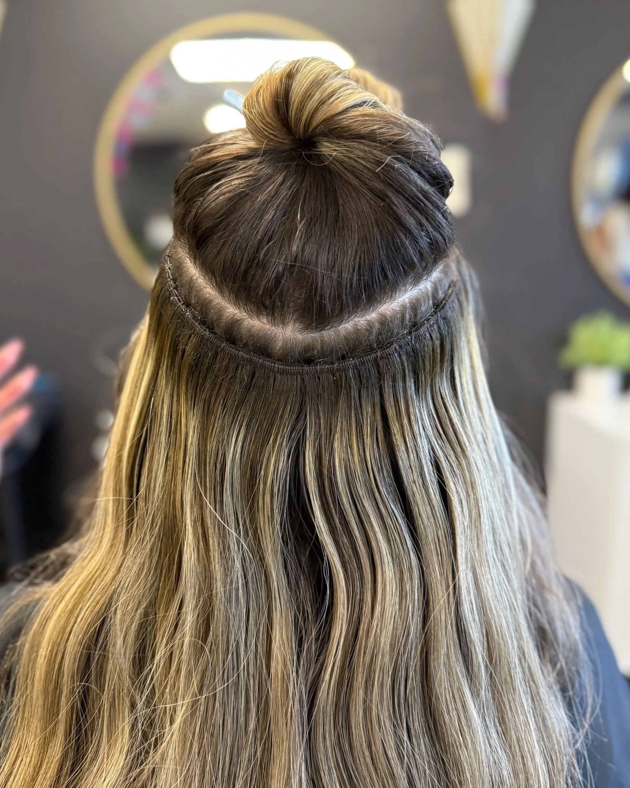 Back of a woman's head with blonde wavy hair, sectioned and held with a headband, in a salon.