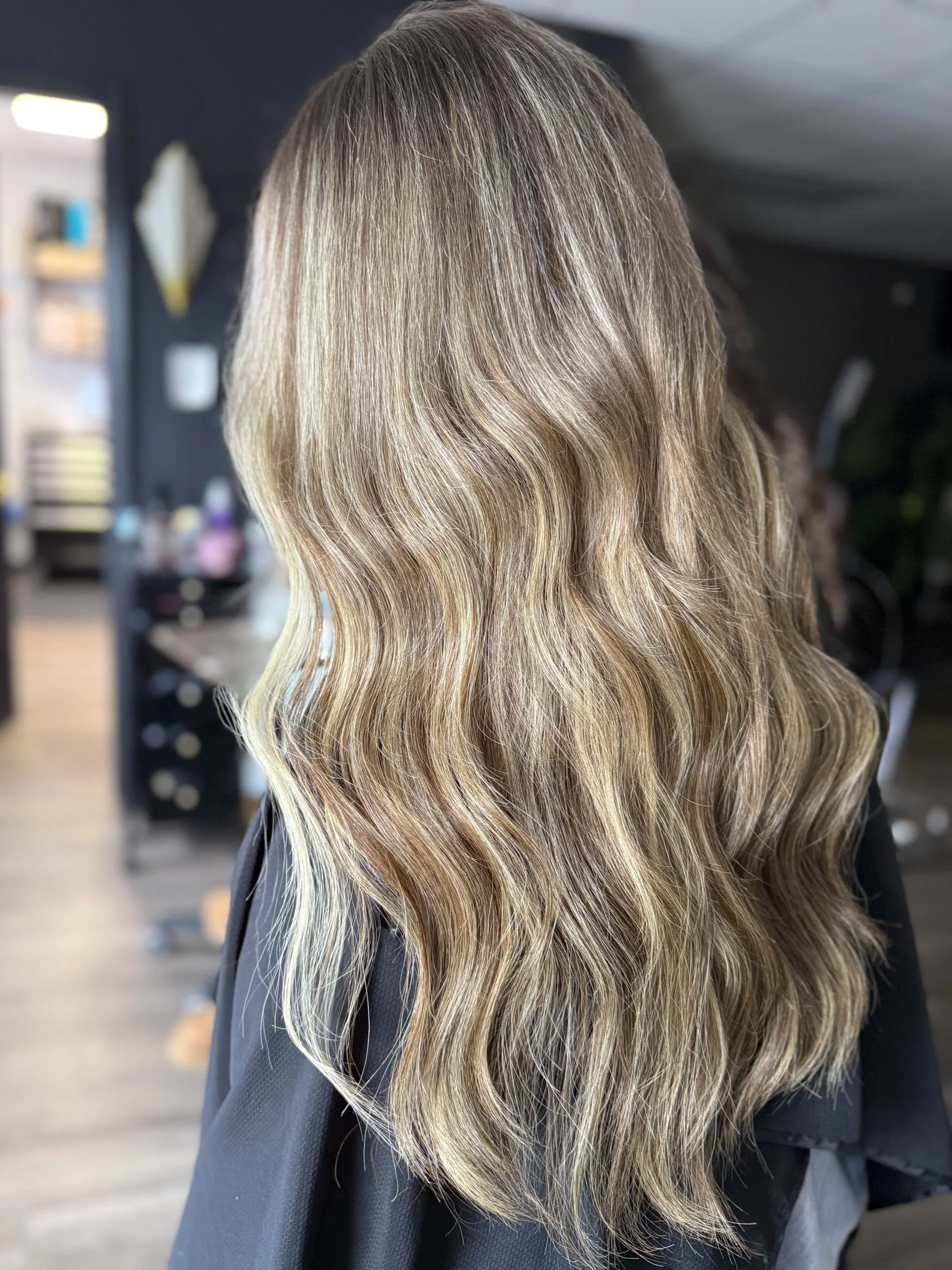 Side view of a person with long, wavy blonde hair in a salon setting.