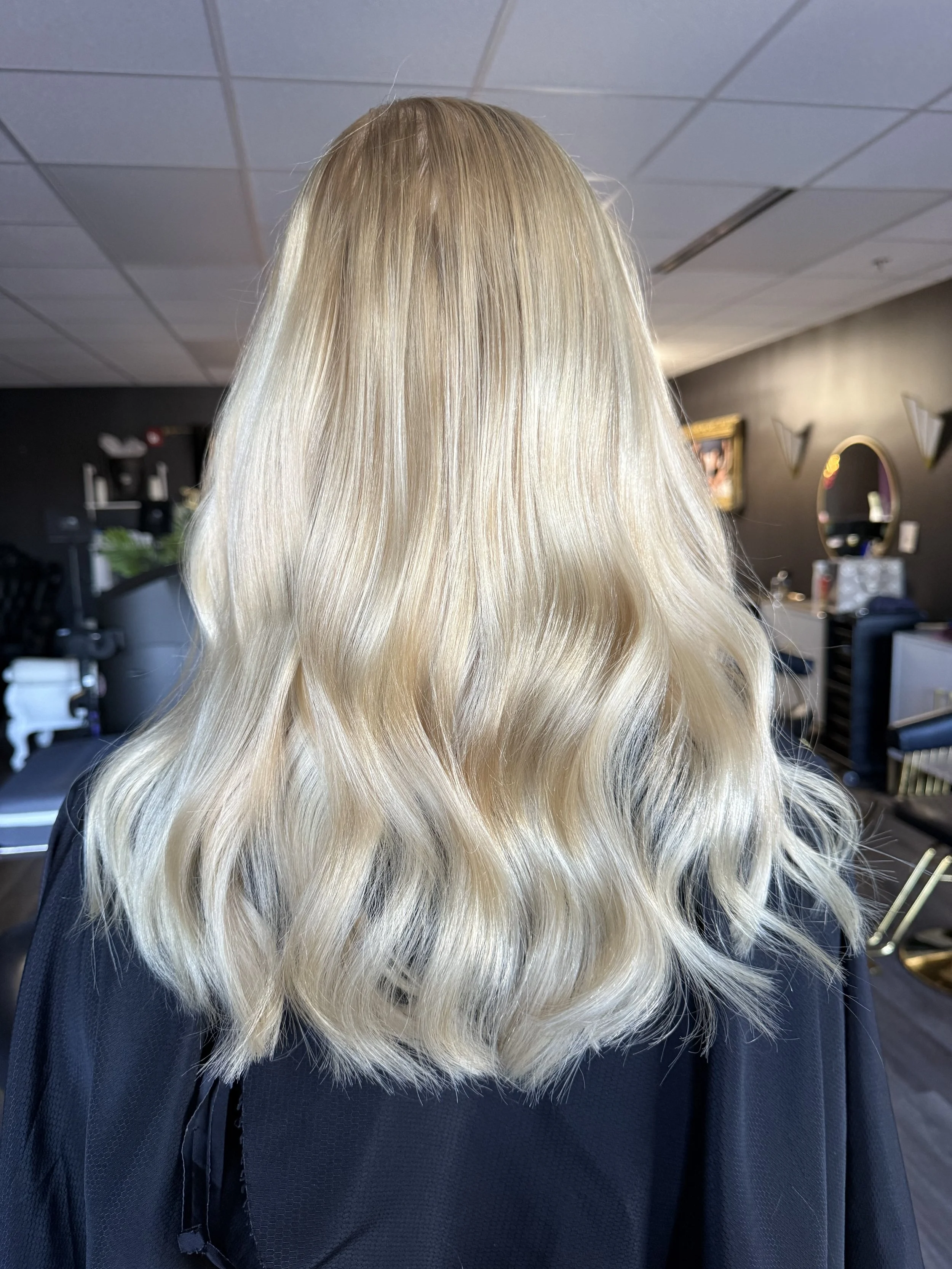 Back of a woman with long, wavy, blonde hair in a salon.
