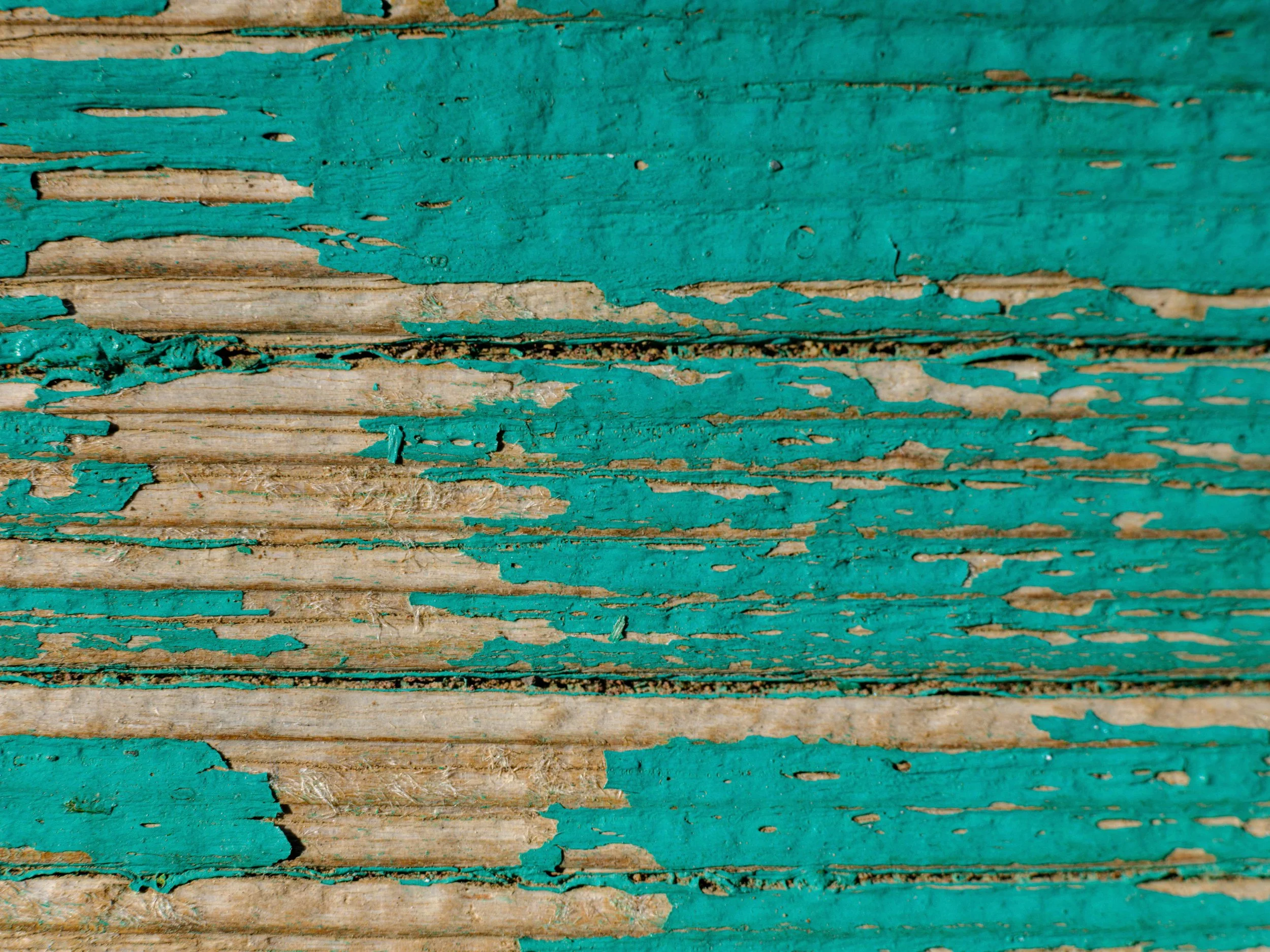 Close-up of weathered wooden surface with peeling turquoise paint.