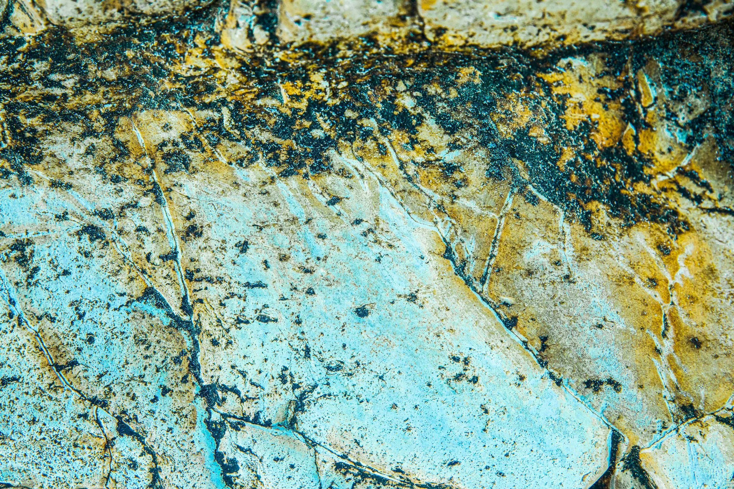 Close-up of a textured, weathered stone surface with cracks and patches of yellow and black mold.